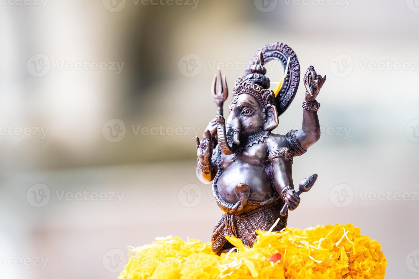 Small replica of Ganesh with iron color is worshiped with a glowing yellow marigold. photo