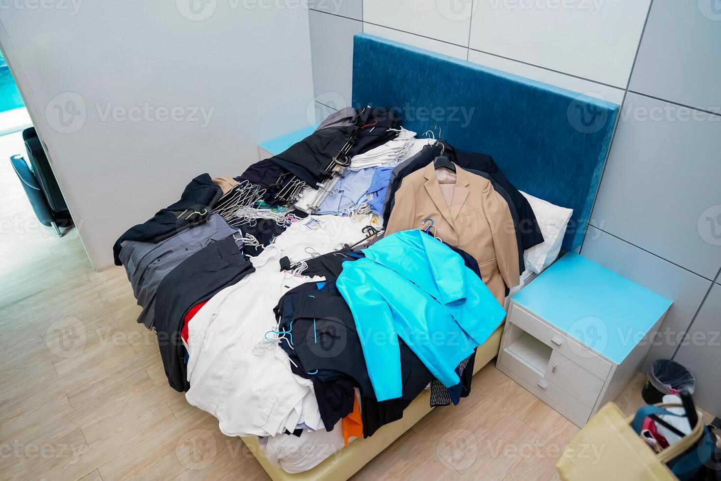 Untidy piles of clothes, arrange on a blue King bed. Women's suits come in a variety of colors, but men's pants were a dark tone color, all of this ready to rearrange in new closet. photo