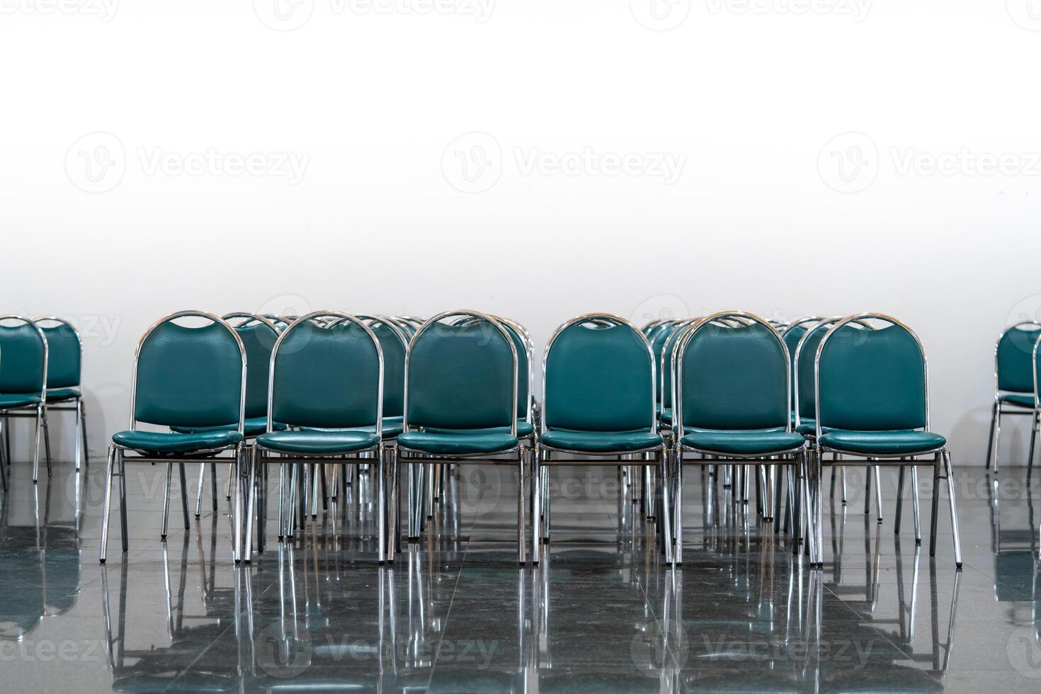 Many empty green leather chairs in a wide hall room, lights on. A floor reflect the objects. Give a feeling of emptiness. photo