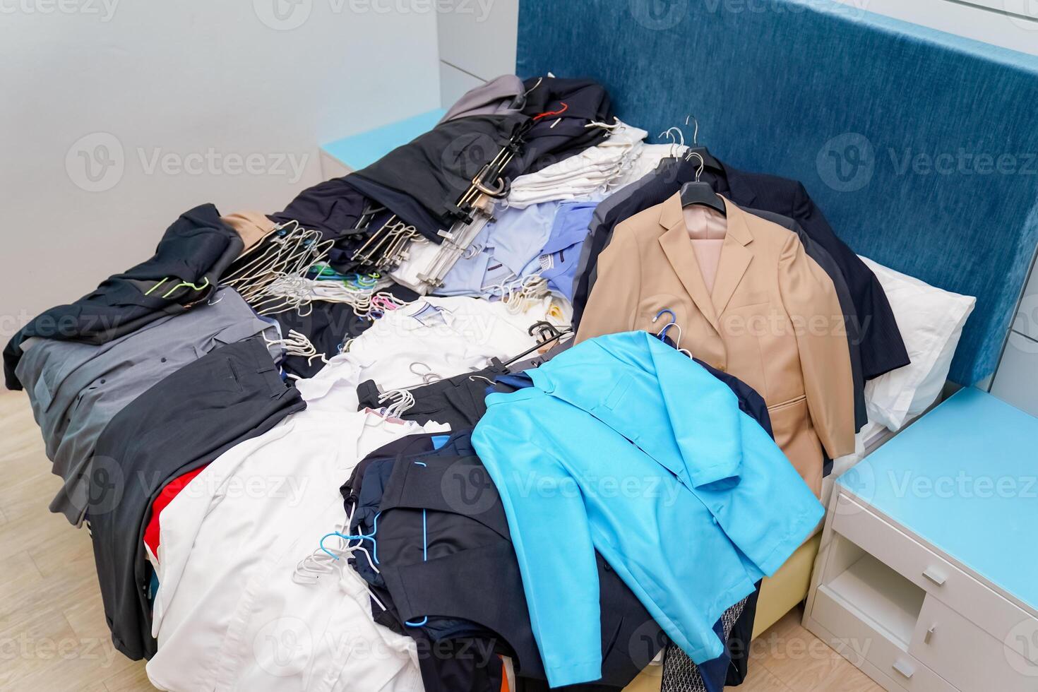 Untidy piles of clothes, arrange on a blue King bed. Women's suits come in a variety of colors, but men's pants were a dark tone color, all of this ready to rearrange in new closet. photo