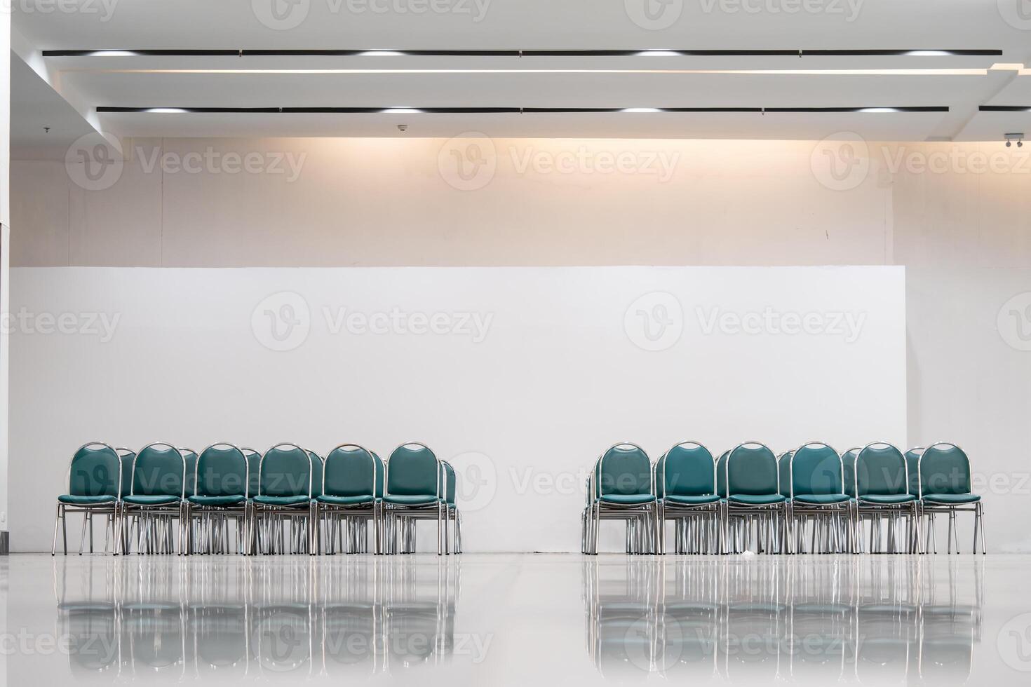 Many empty green leather chairs in a wide hall room, lights on. A floor reflect the objects. Give a feeling of emptiness. photo