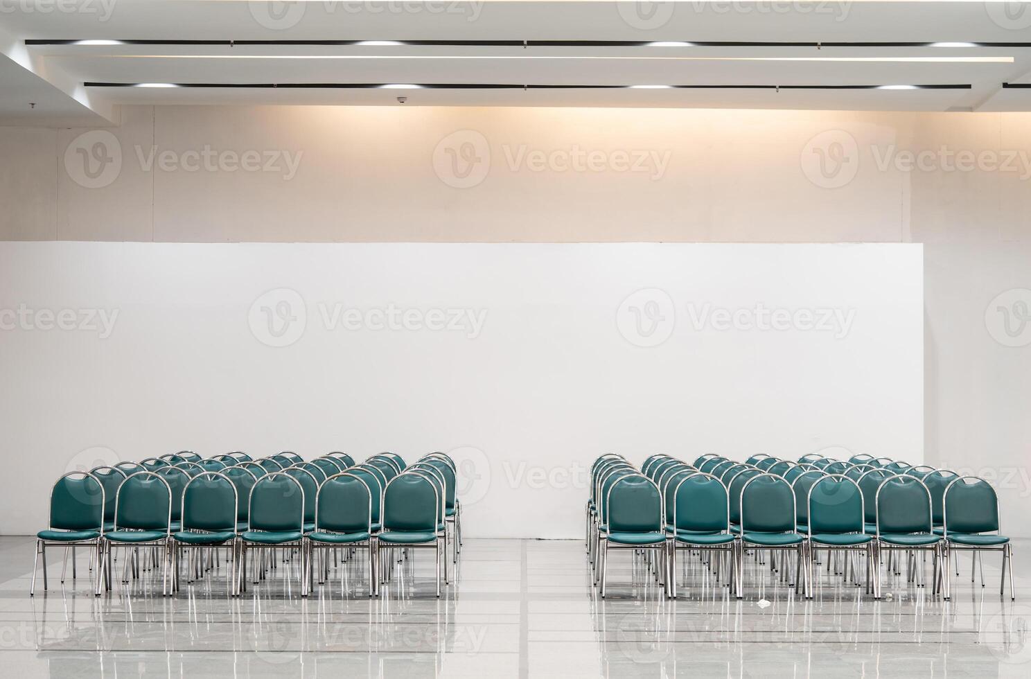 Many empty green leather chairs in a wide hall room, lights on. A floor reflect the objects. Give a feeling of emptiness. photo