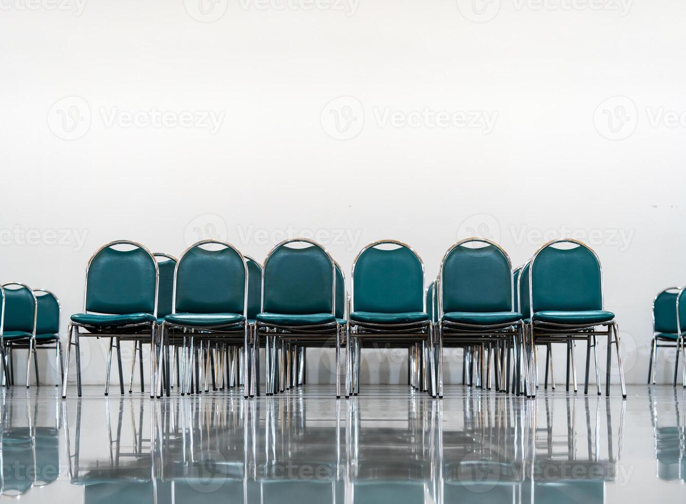 Many empty green leather chairs in a wide hall room, lights on. A floor reflect the objects. Give a feeling of emptiness. photo