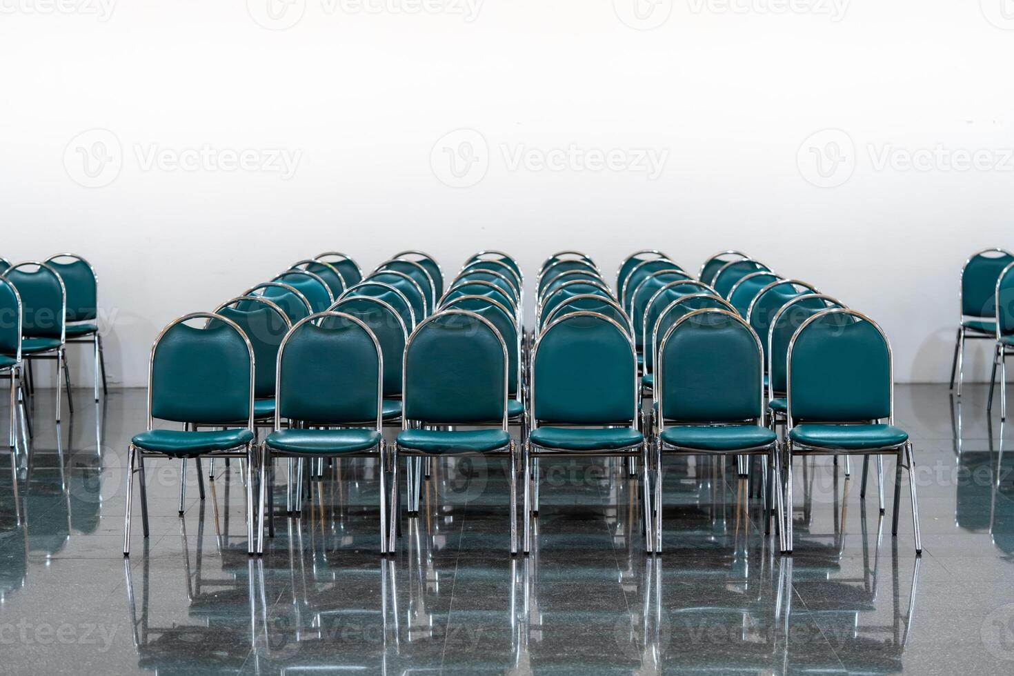 Many empty green leather chairs in a wide hall room, lights on. A floor reflect the objects. Give a feeling of emptiness. photo