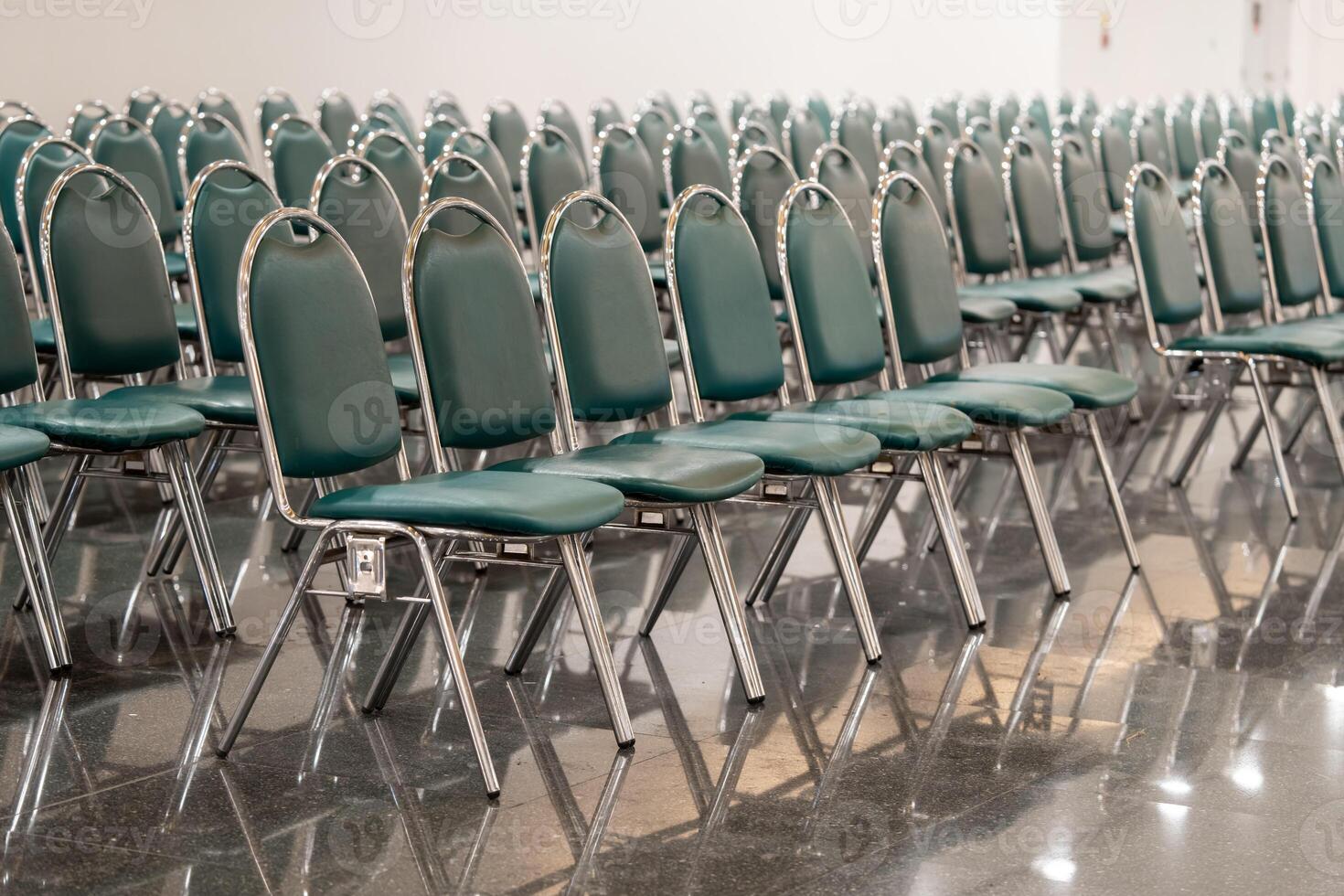 Many empty green leather chairs in a wide hall room, lights on. A floor reflect the objects. Give a feeling of emptiness. photo
