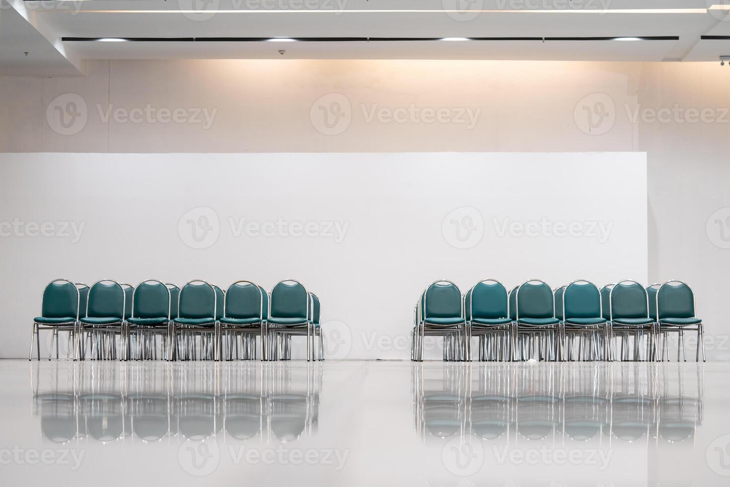 Many empty green leather chairs in a wide hall room, lights on. A floor reflect the objects. Give a feeling of emptiness. photo