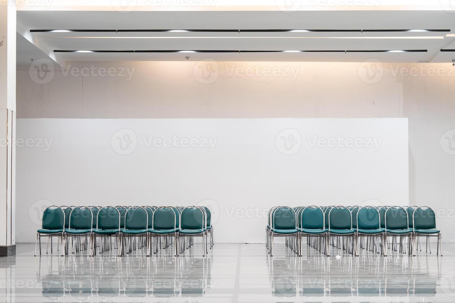 Many empty green leather chairs in a wide hall room, lights on. A floor reflect the objects. Give a feeling of emptiness. photo