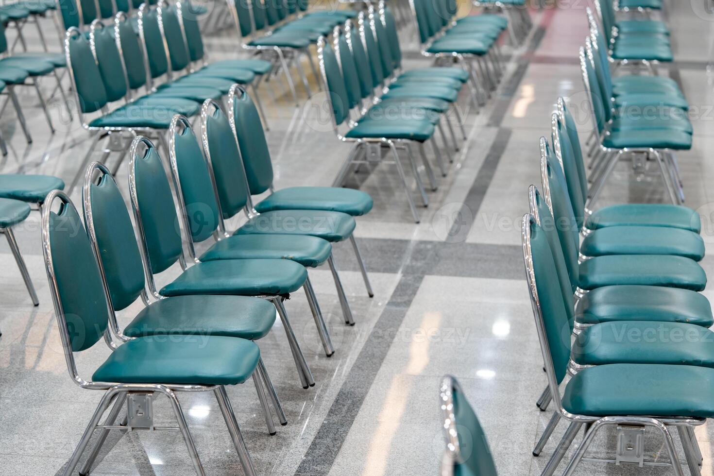 Many empty green leather chairs in a wide hall room, lights on. A floor reflect the objects. Give a feeling of emptiness. photo