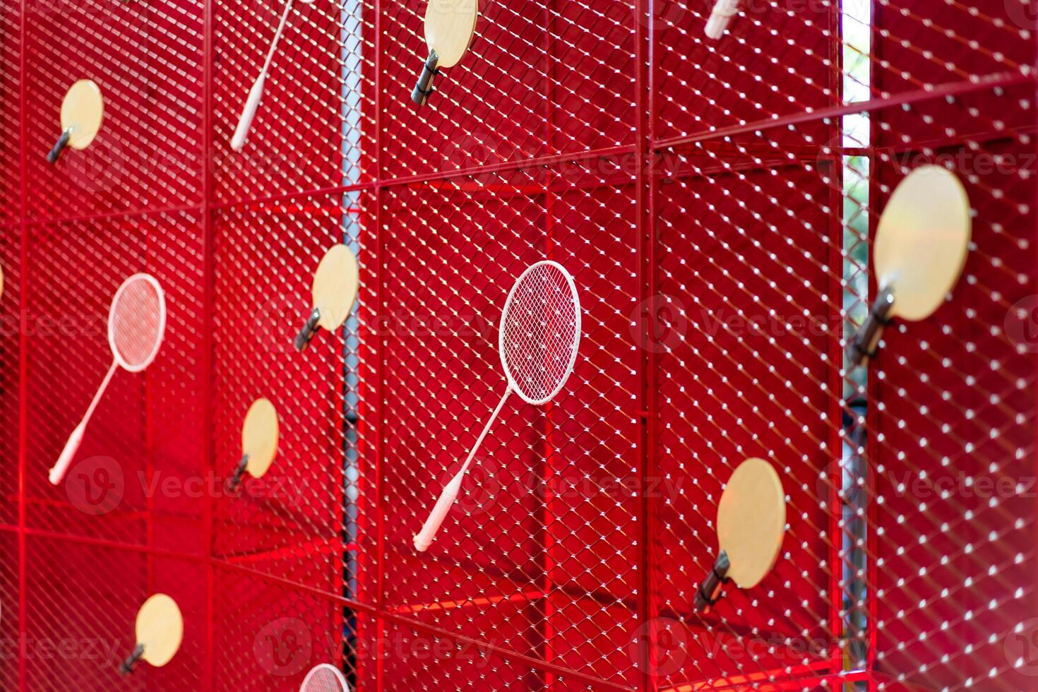 Table tennis and badminton rackets are hung on a red square grill steel grid, used as a backdrop for various events. photo