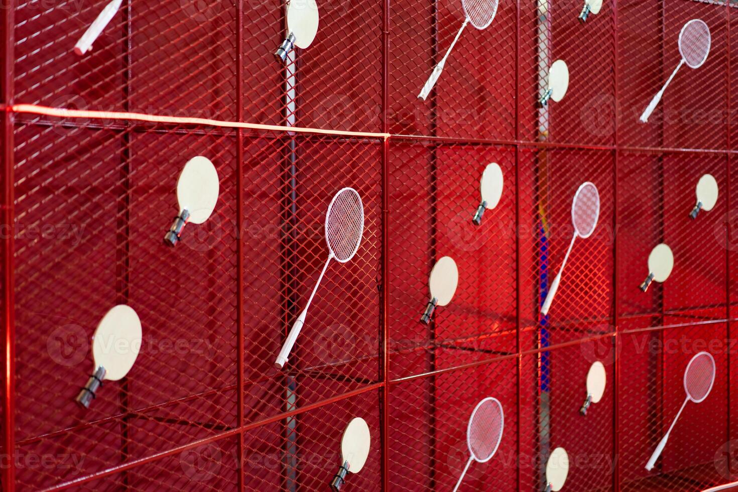 Table tennis and badminton rackets are hung on a red square grill steel grid, used as a backdrop for various events. photo