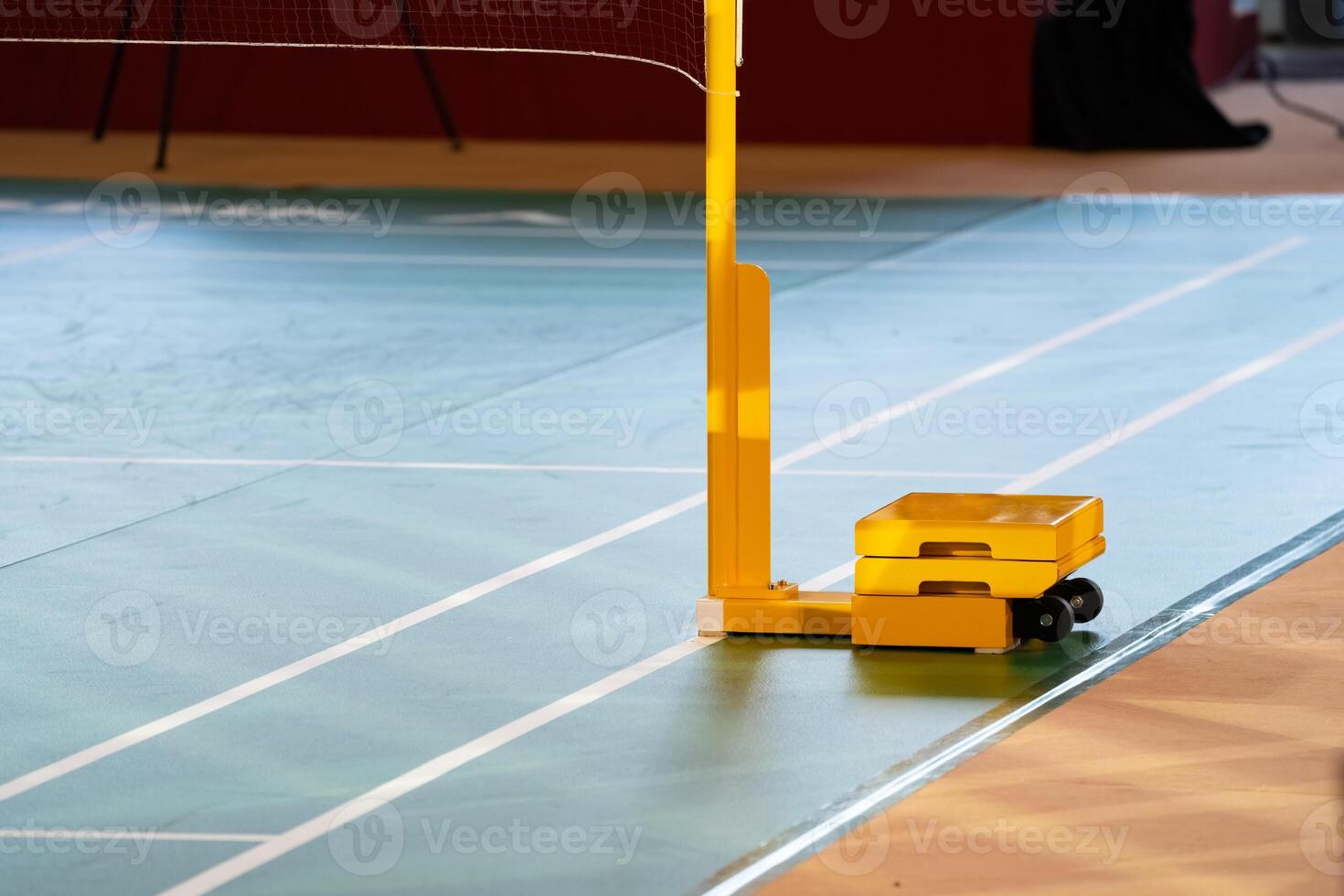 Yellow weighted pole badminton net base was placed on the side of a badminton court. photo