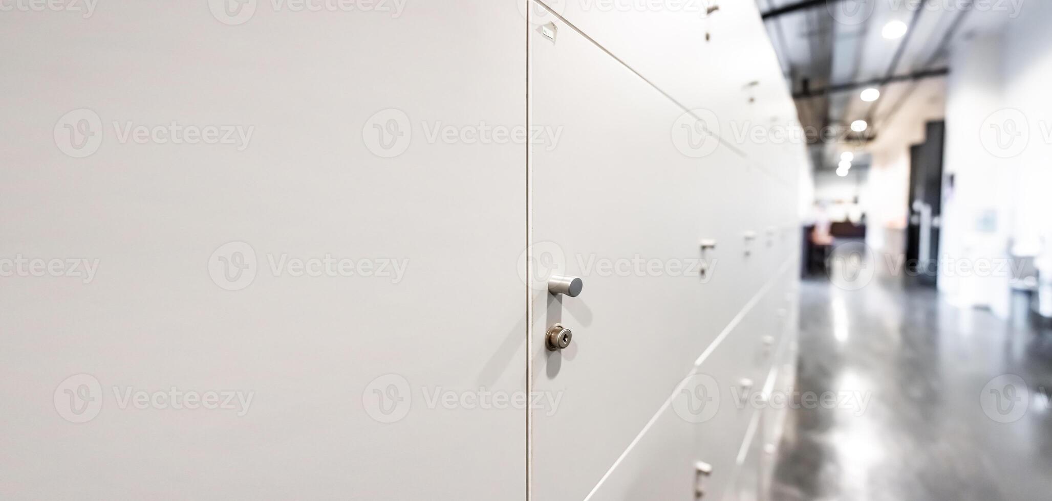 Large gray locker with each locker closed located beside corridors inside building are dimly lit. photo