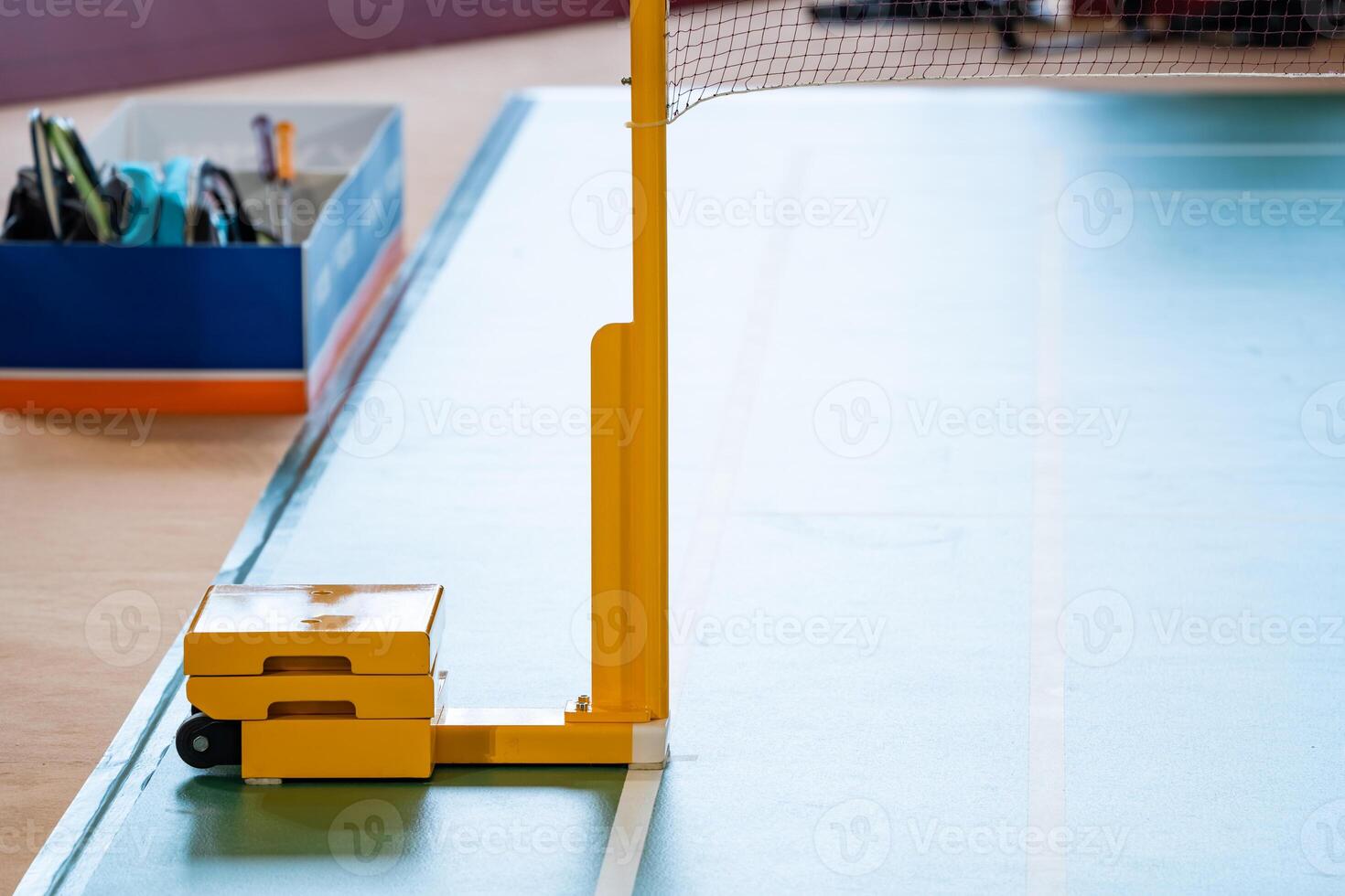 Yellow weighted pole badminton net base was placed on the side of a badminton court. photo