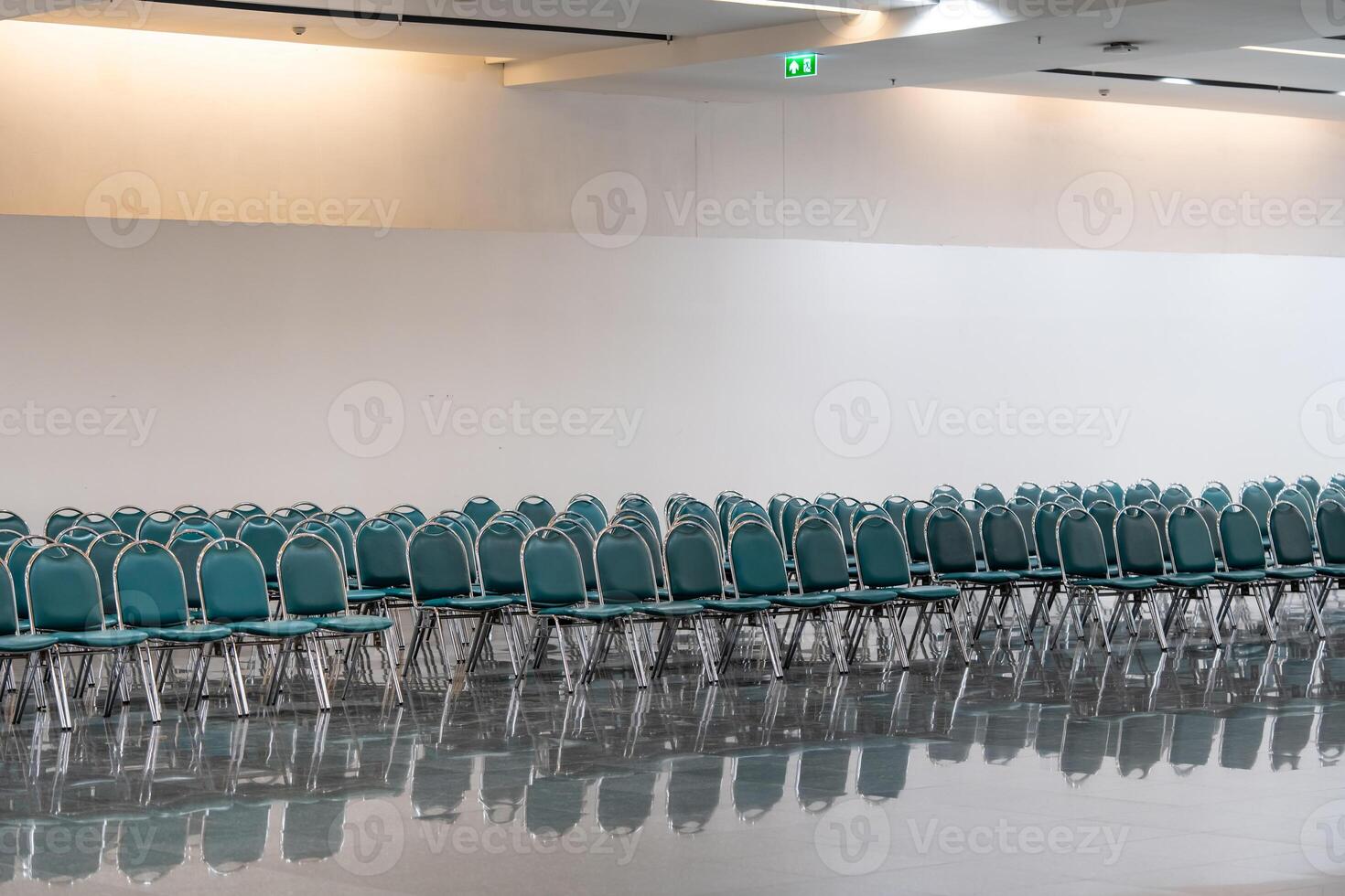 Many empty green leather chairs in a wide hall room, lights on. A floor reflect the objects. Give a feeling of emptiness. photo