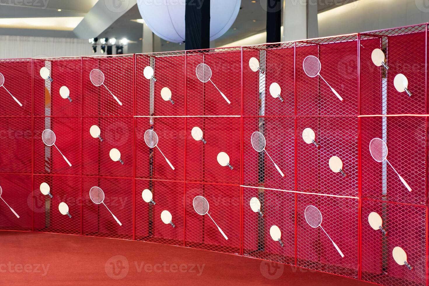 Table tennis and badminton rackets are hung on a red square grill steel grid, used as a backdrop for various events. photo
