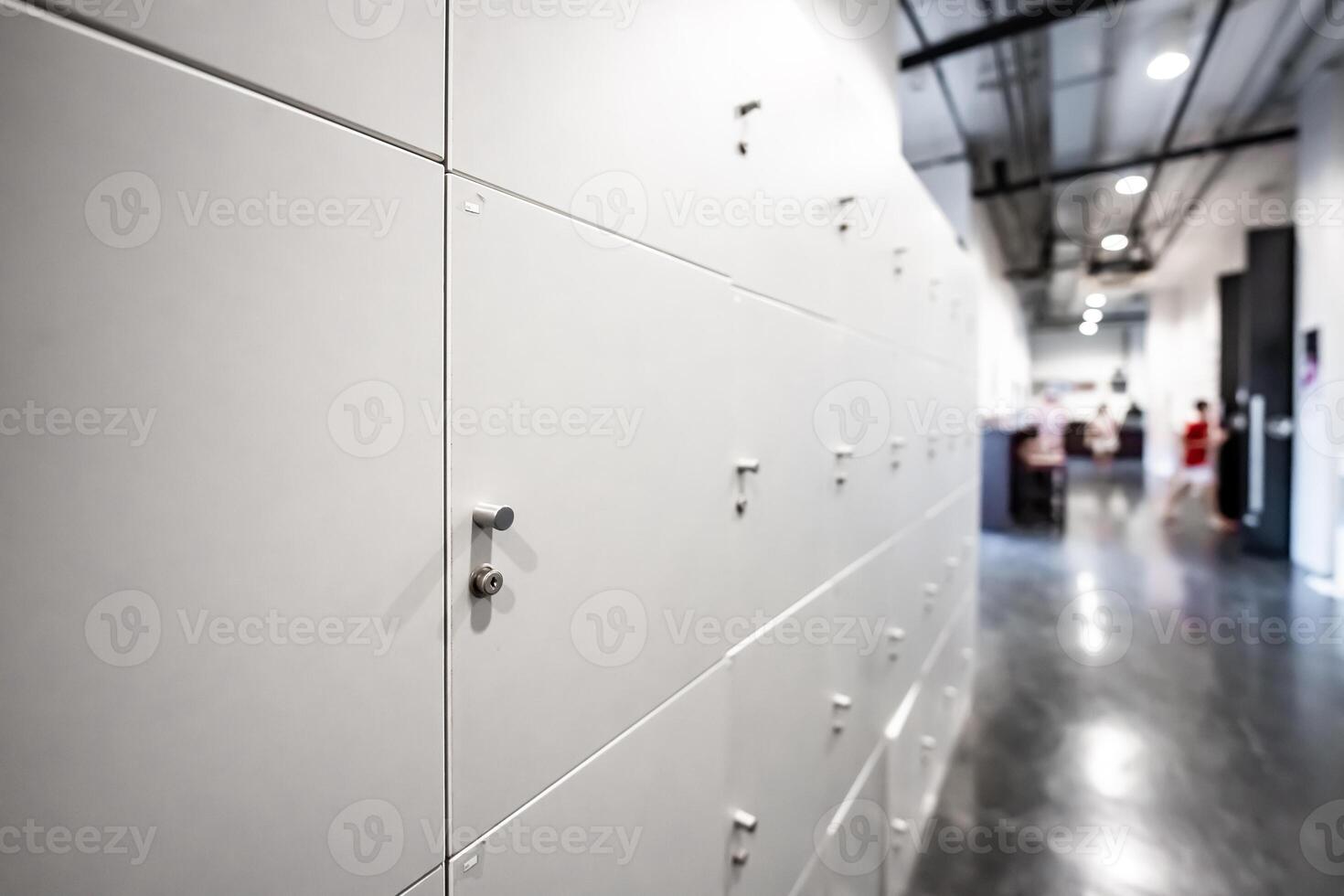 Large gray locker with each locker closed located beside corridors inside building are dimly lit. photo