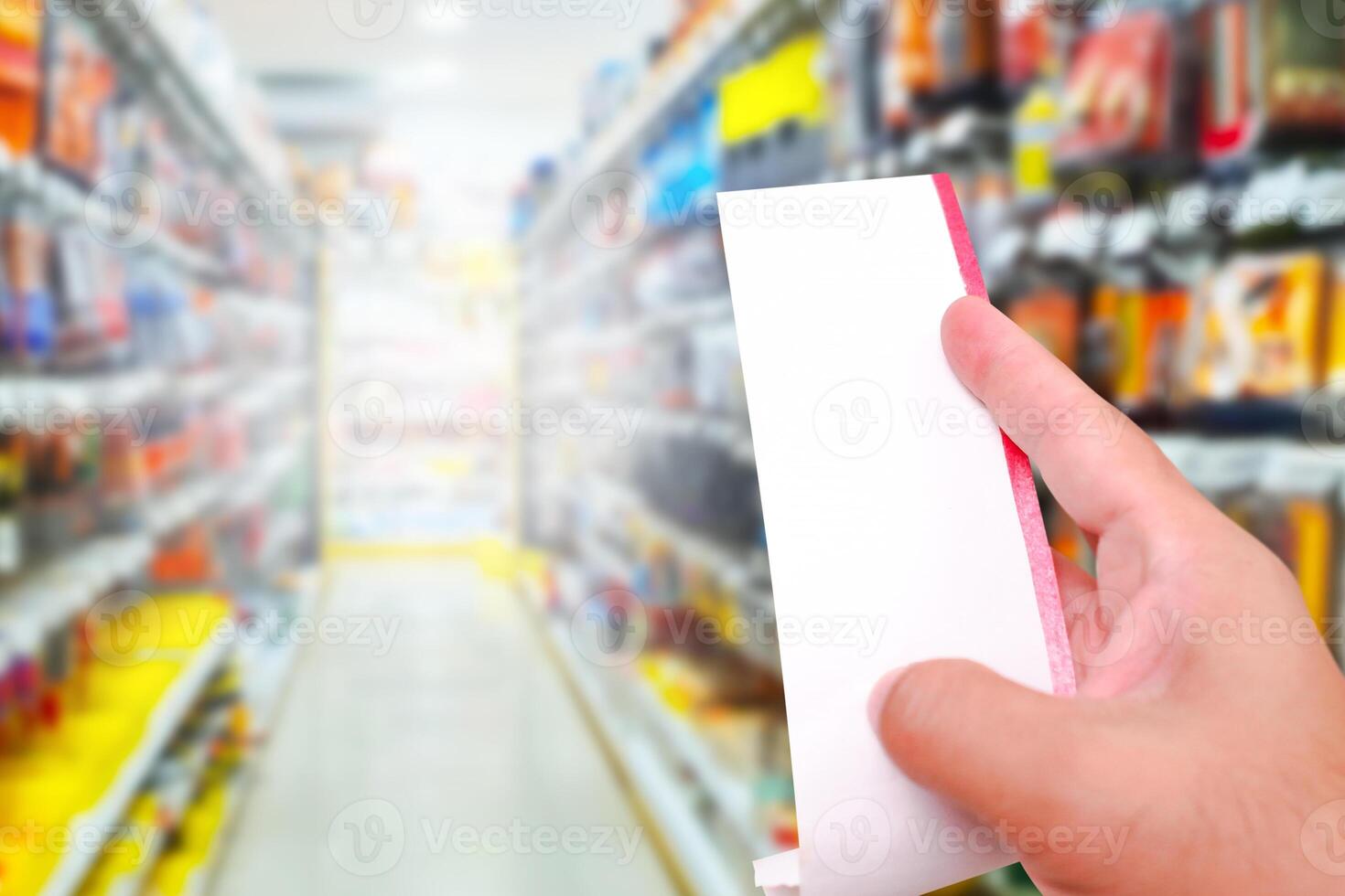 Blank white bill in a hand with product shelf blurred on background at shopping mall , shopping and payment concept photo