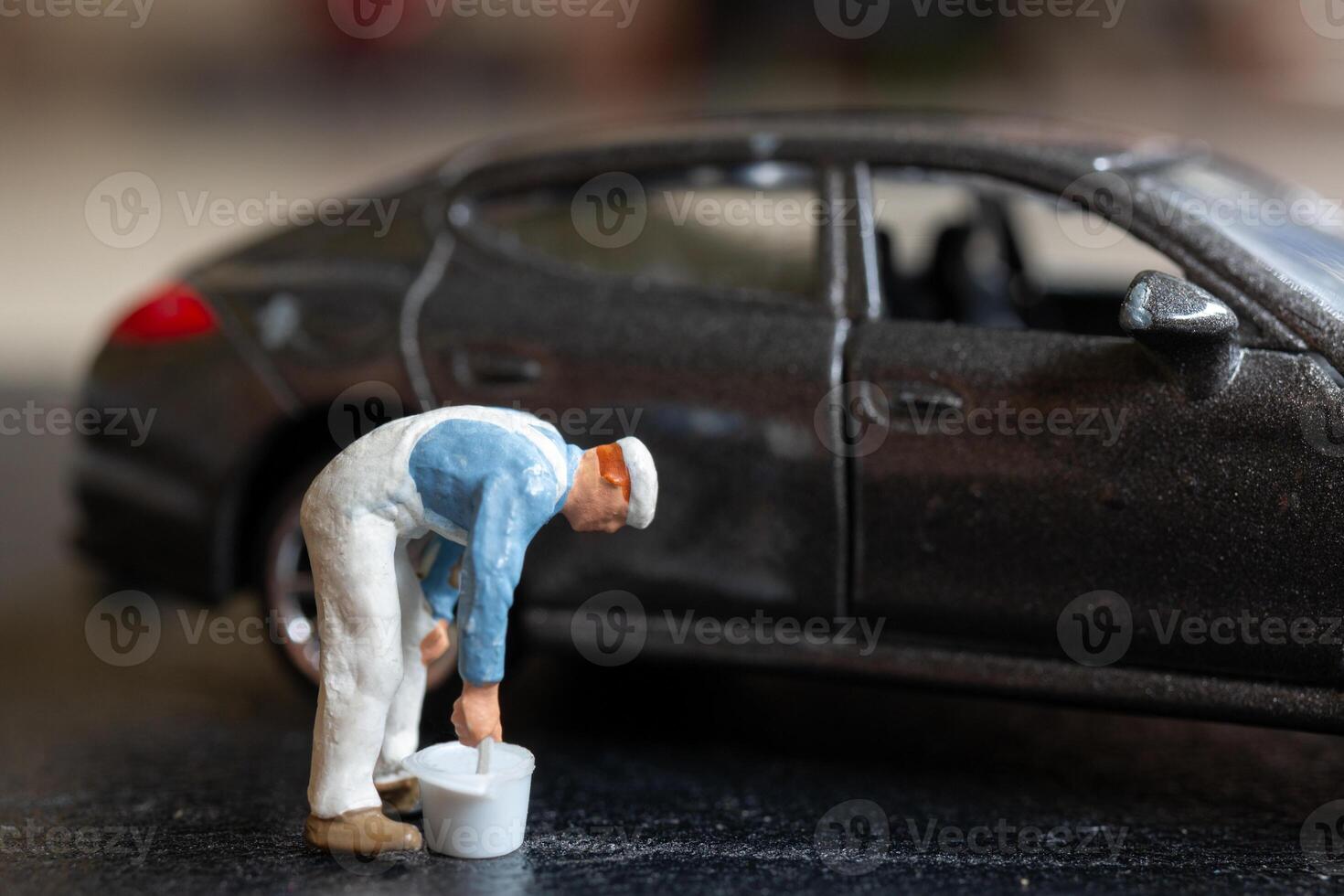 Miniature people, A worker bends over as if inspecting or repairing something on a sleek metallic gray car model photo