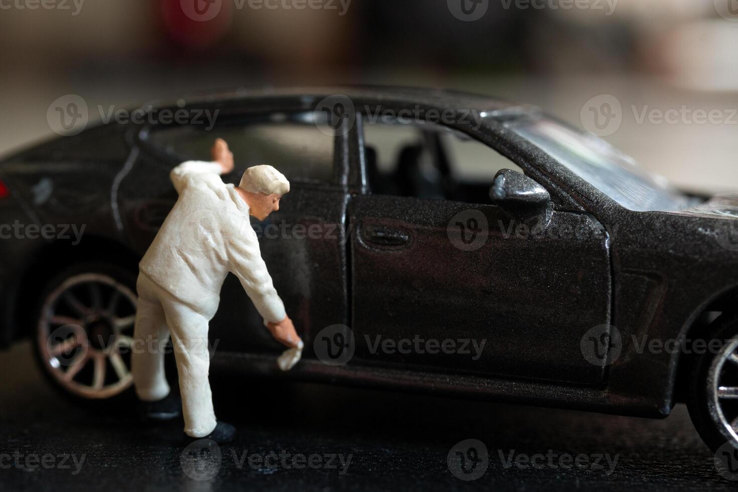 Miniature people, A worker bends over as if inspecting or repairing something on a sleek metallic gray car model photo