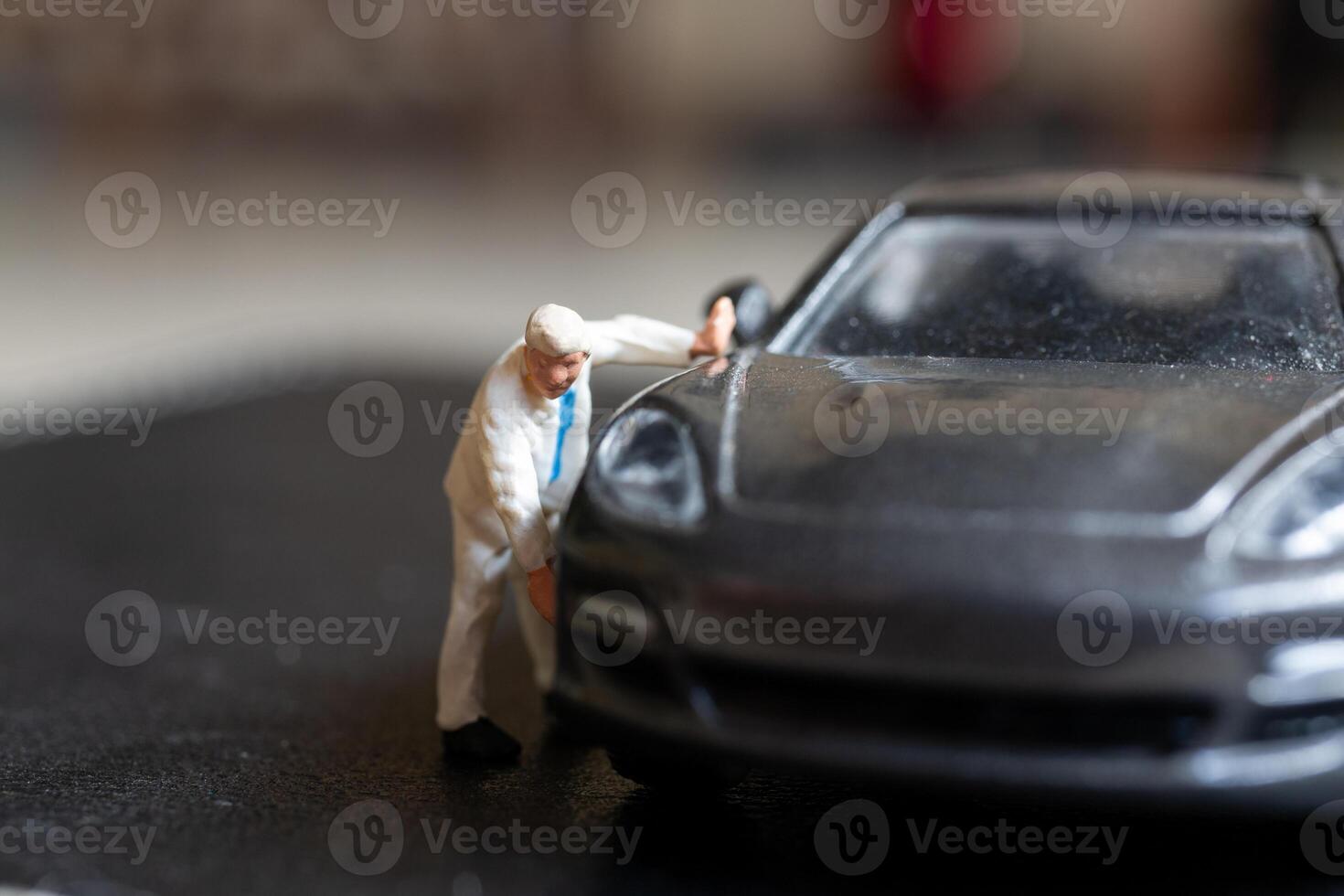 Miniature people, A worker bends over as if inspecting or repairing something on a sleek metallic gray car model photo