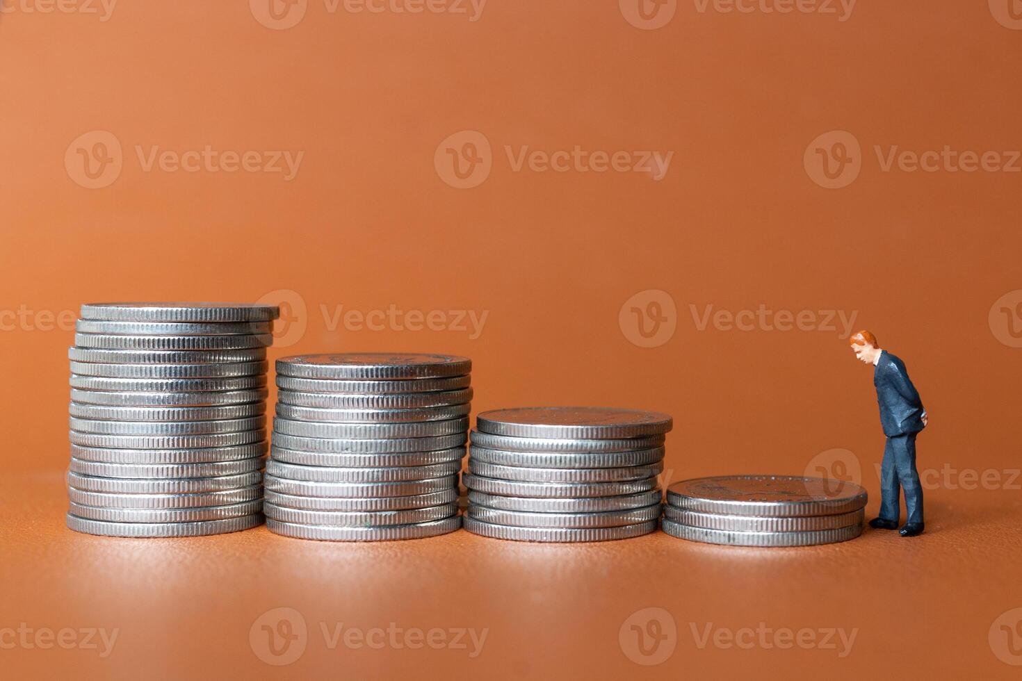 Miniature people A businessman in a suit stands with several stacks of silver coins photo