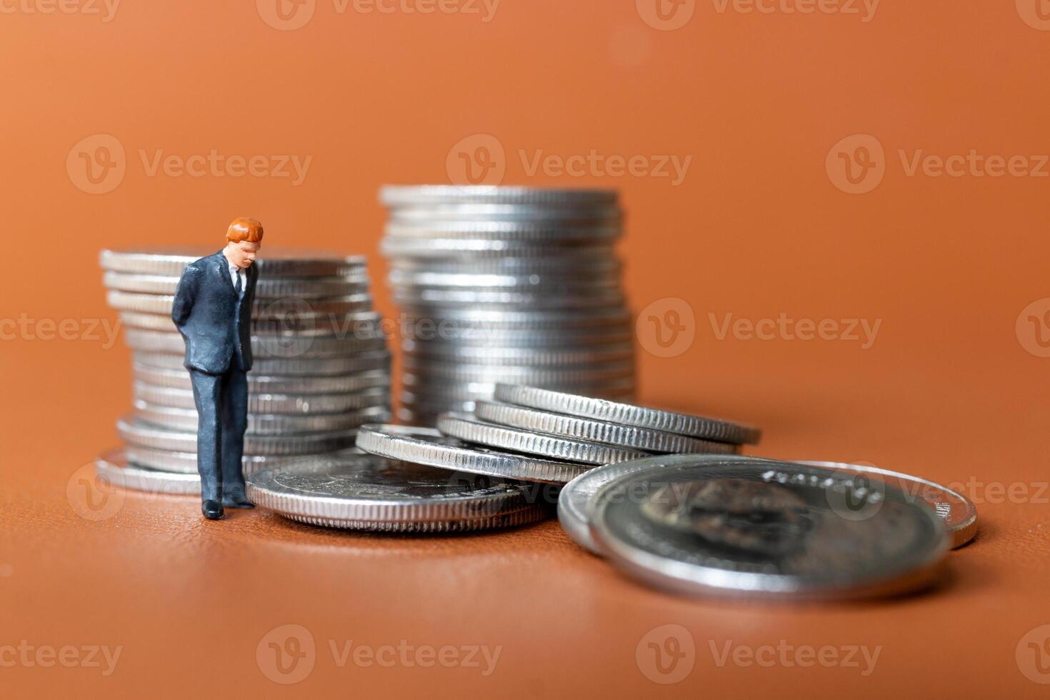 Miniature people A businessman in a suit stands with several stacks of silver coins photo
