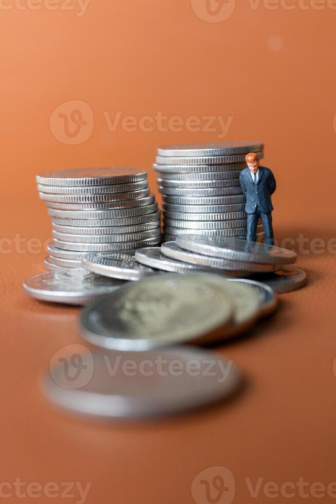 Miniature people A businessman in a suit stands with several stacks of silver coins photo