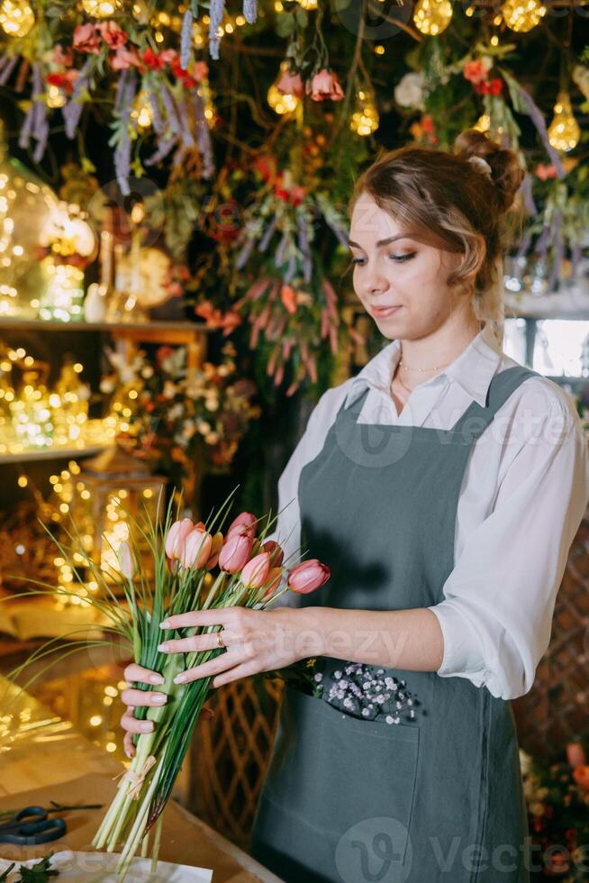 A woman in her florist shop collects bouquets of flowers. The concept of a small business. Bouquets of tulips for the holiday on March 8. photo