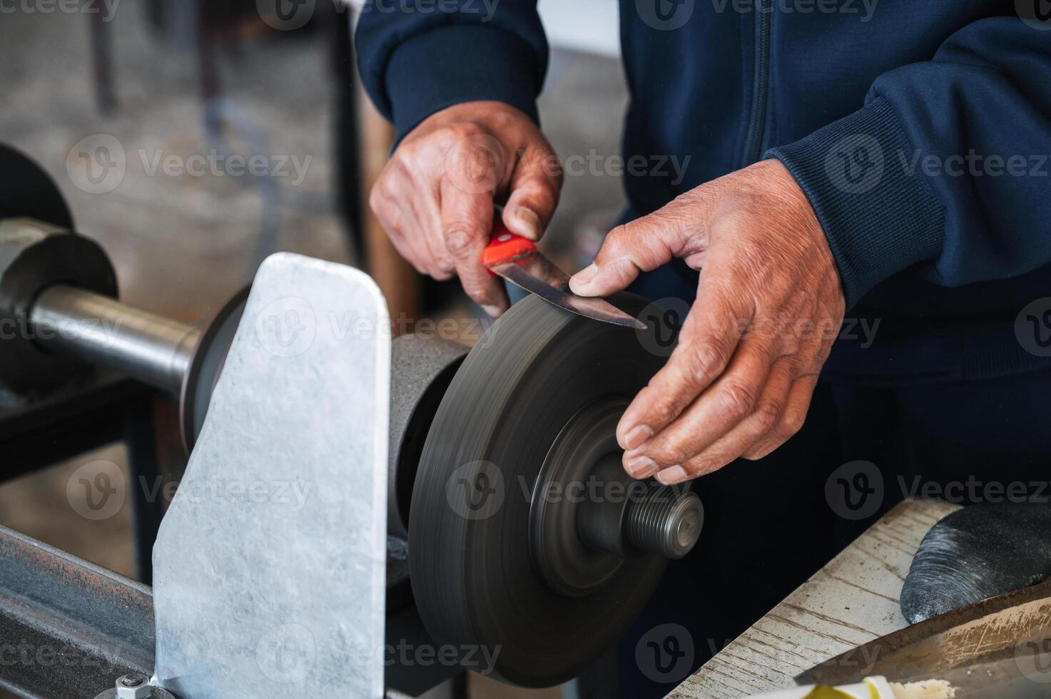 male sharpener grinder sharpens knife blade on sharpening machine with rotating abrasive wheel close-up photo