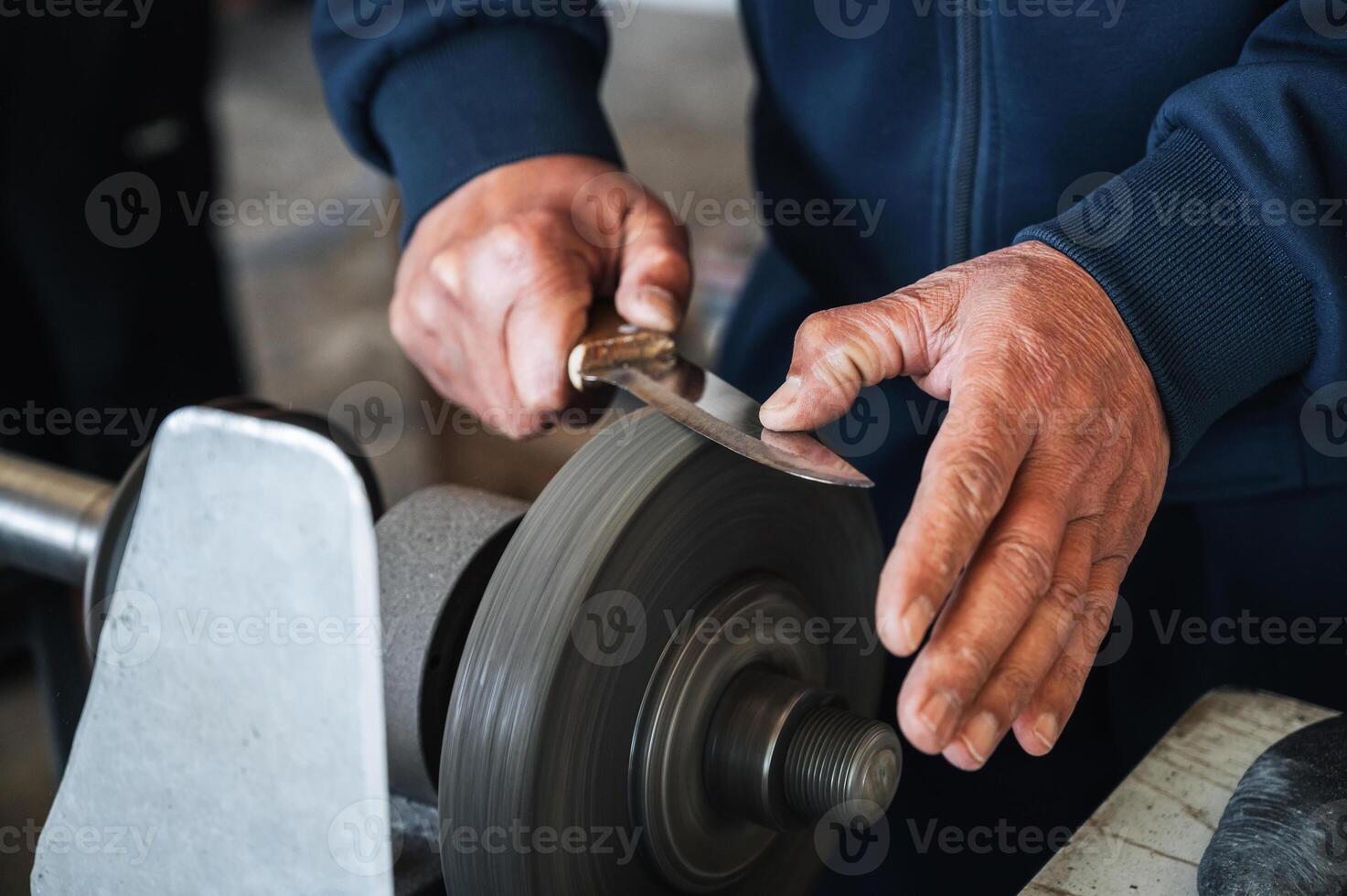 hands of grinder male sharpener sharpening a knife blade on a grinding machine with abrasive wheel in the workshop close-up photo