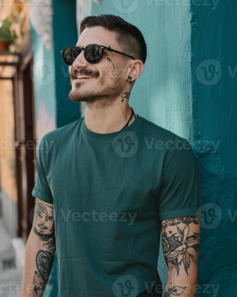 A man wearing a green t-shirt smiles while leaning against a wall photo