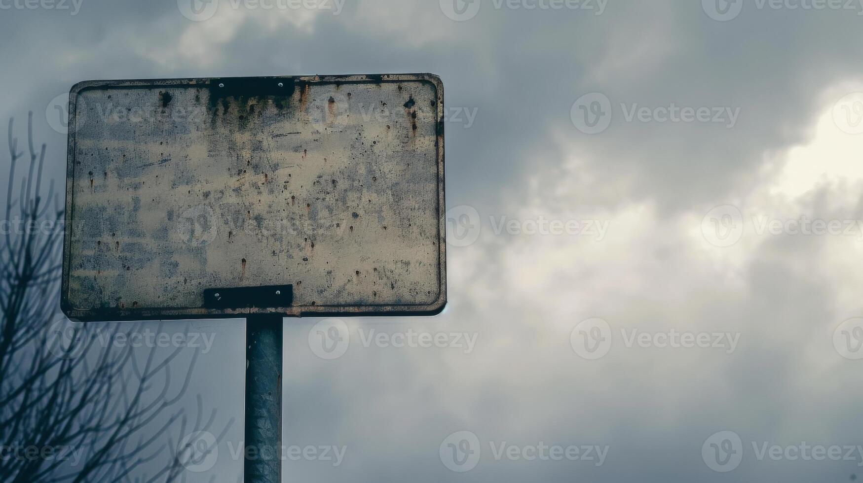 A weathered sign stands tall against a cloudy sky photo