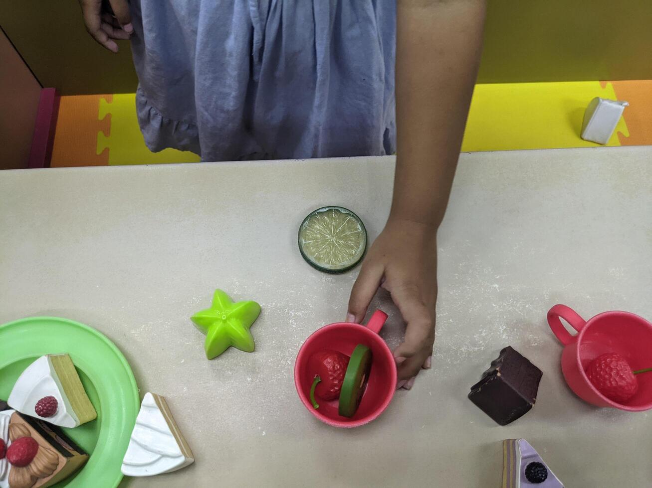 Child Playing with Play Food. A young child playing with plastic toy food, setting a table with cakes and fruit. photo