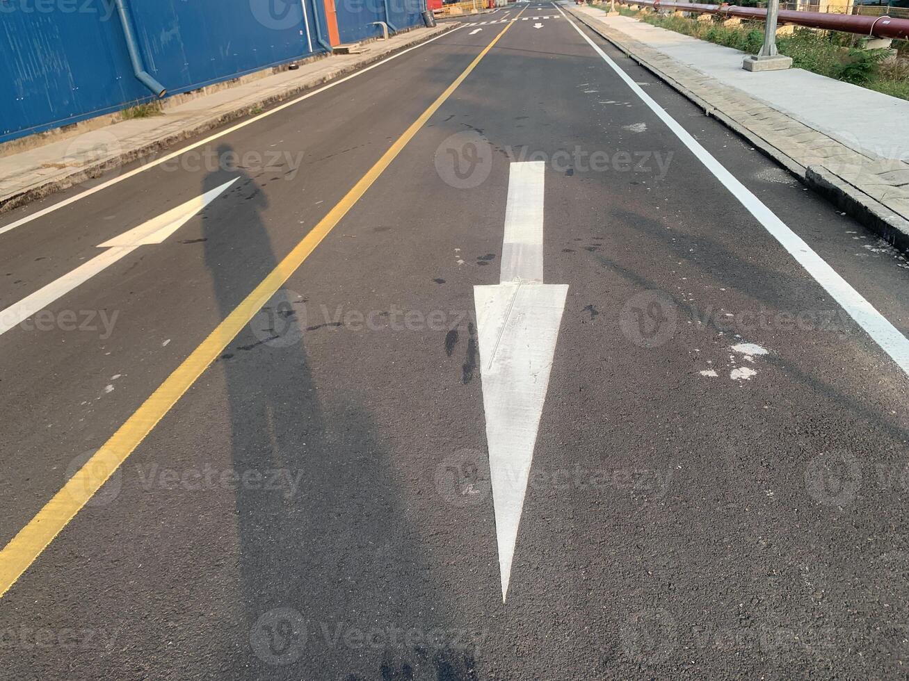 Road Marking with a White Arrow. A close-up view of white painted arrows on a grey asphalt road. The arrows indicate direction and guidance for vehicles. photo