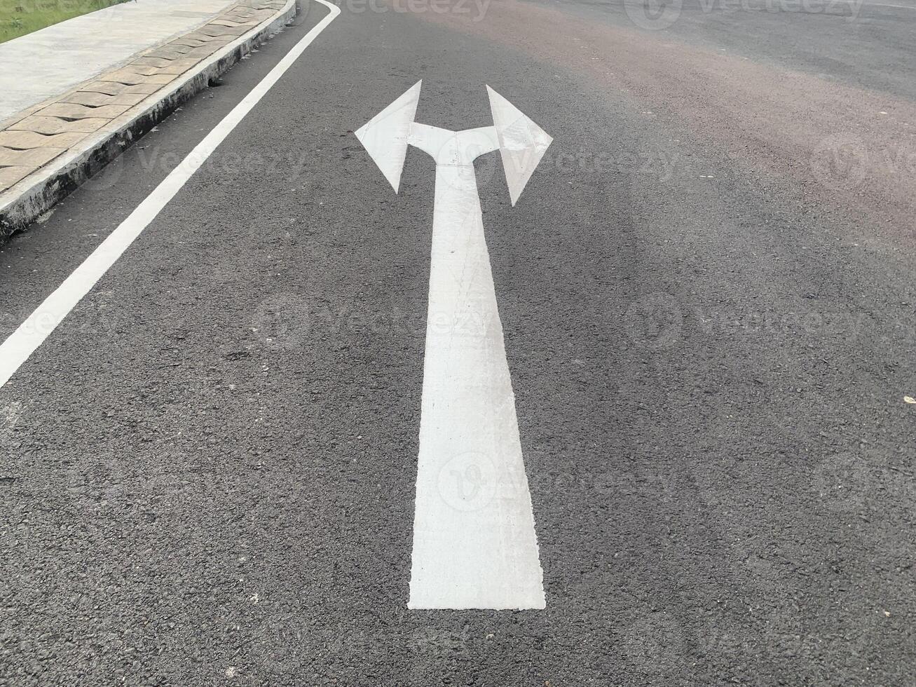 Road Marking with a White Arrow. A close-up view of white painted arrows on a grey asphalt road. The arrows indicate direction and guidance for vehicles. photo