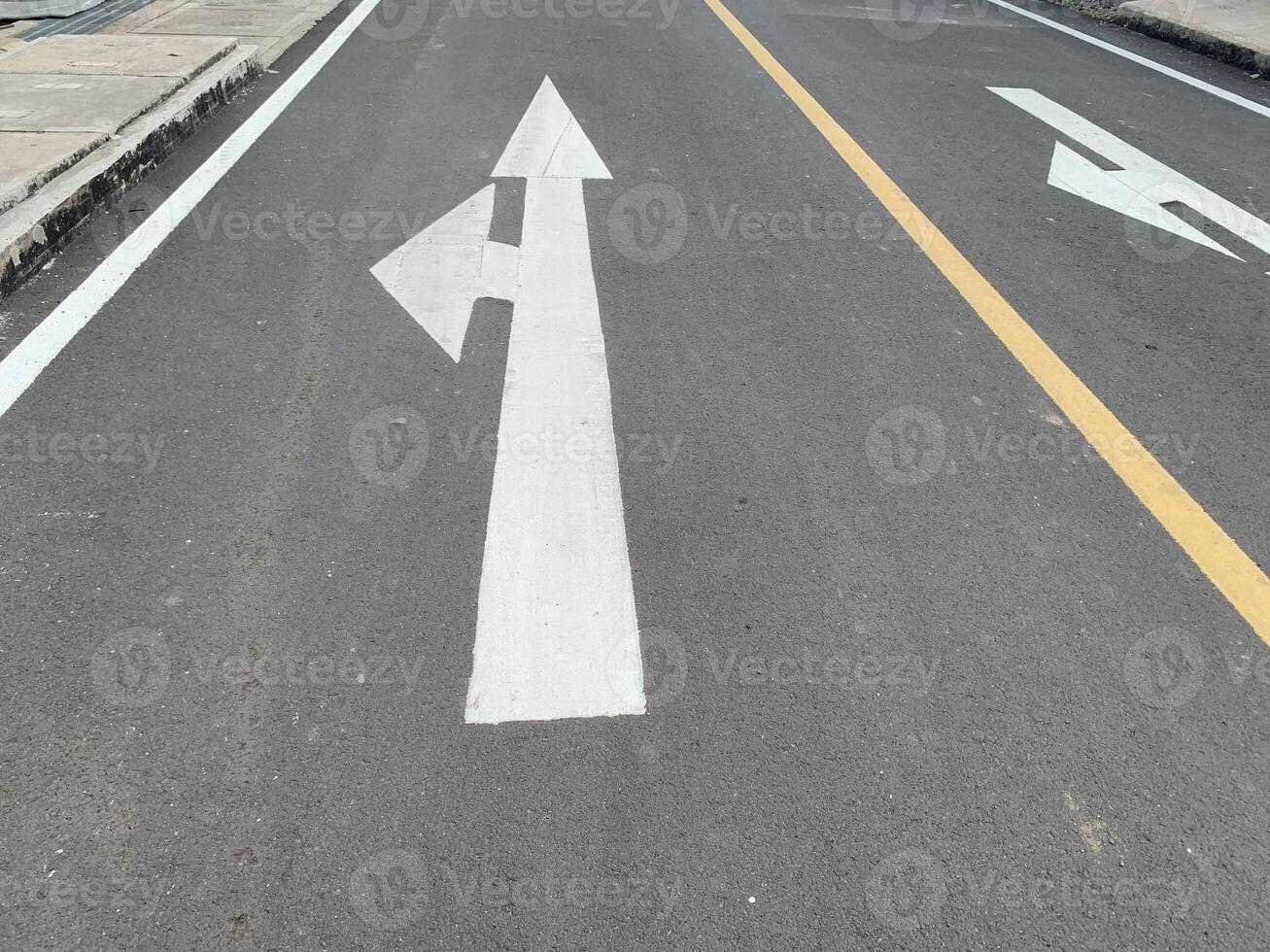 Road Marking with a White Arrow. A close-up view of white painted arrows on a grey asphalt road. The arrows indicate direction and guidance for vehicles. photo