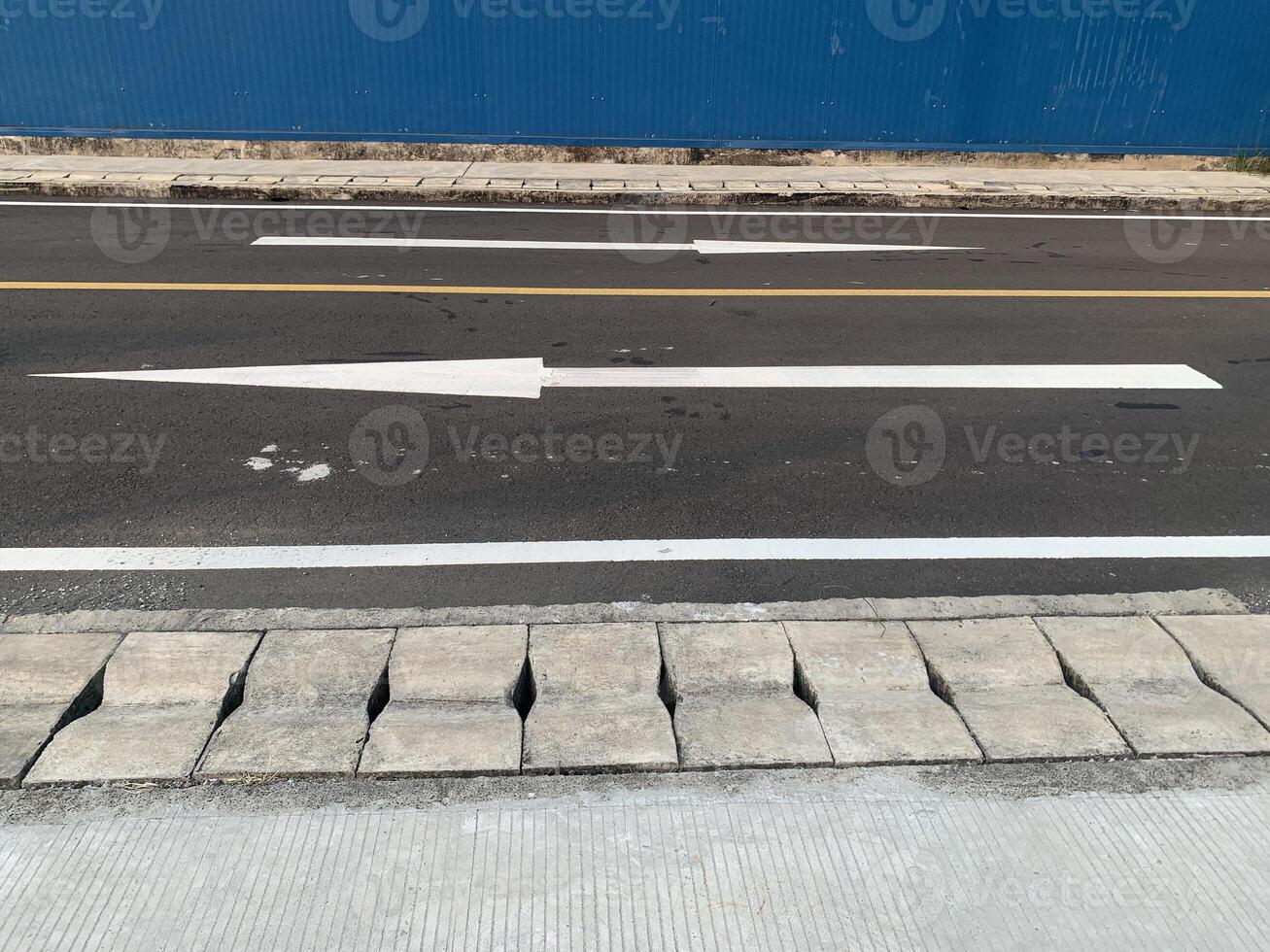 Road Marking with a White Arrow. A close-up view of white painted arrows on a grey asphalt road. The arrows indicate direction and guidance for vehicles. photo