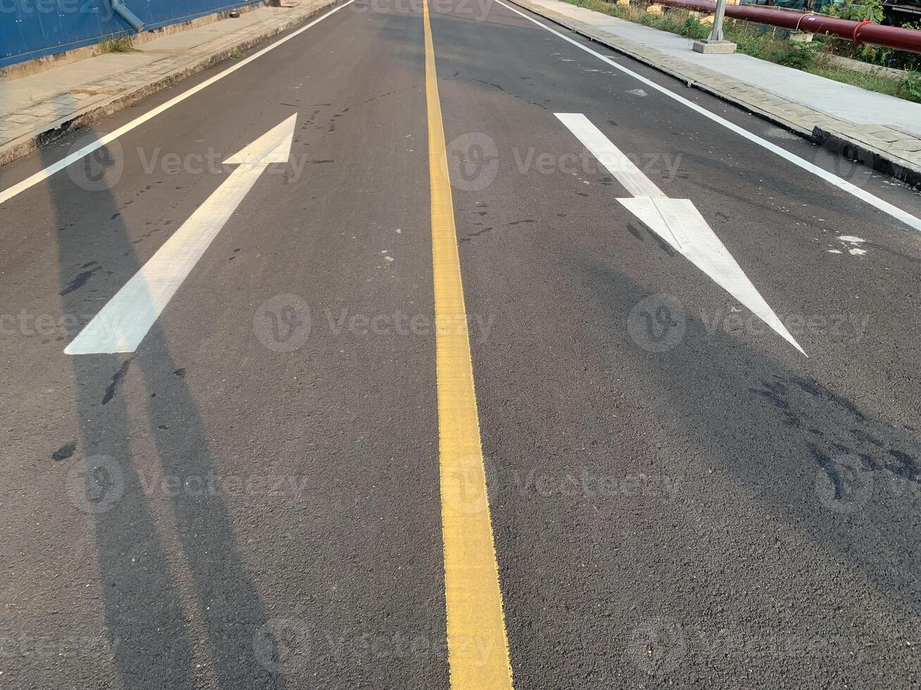 Road Marking with a White Arrow. A close-up view of white painted arrows on a grey asphalt road. The arrows indicate direction and guidance for vehicles. photo