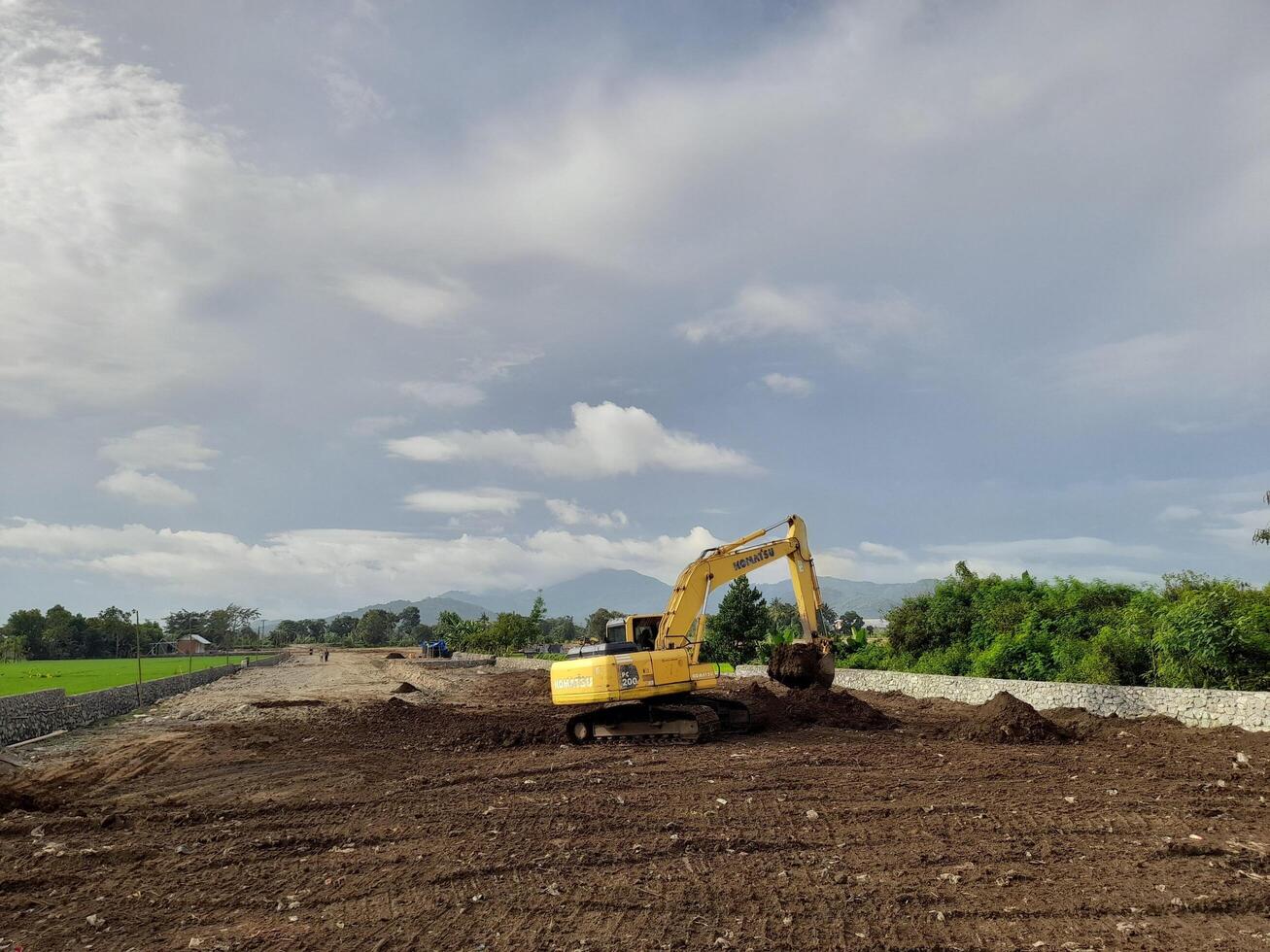 West Lombok Regency, Indonesia - February 4, 2024. Outdoors, a Backhoe is at work leveling the ground for a housing site, with a blue sky in the background. photo