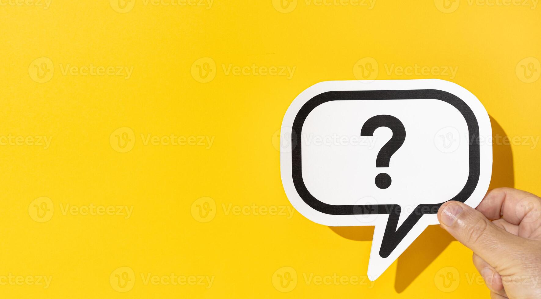 Hand holding a question mark on speech bubble on yellow background. Copy space photo