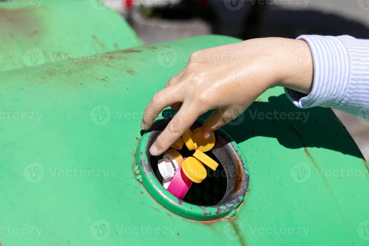 Female Hand throwing plastic bottle caps into an urban recycling bin. Recycle and reuse concept for an environmentally and globally friendly approach photo