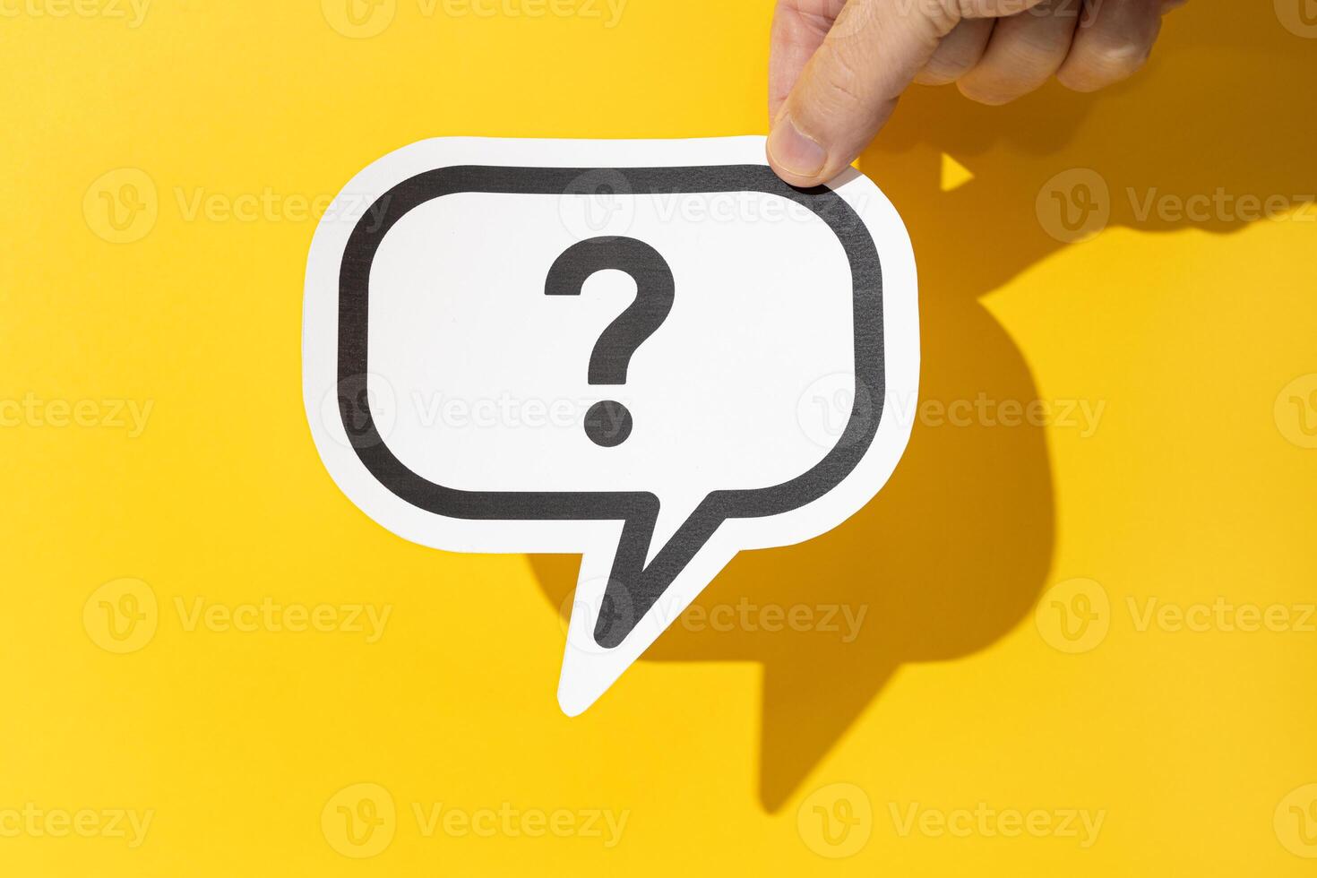 Hand holding a question mark on speech bubble on yellow background. Doubt, confusion, uncertainty concept photo