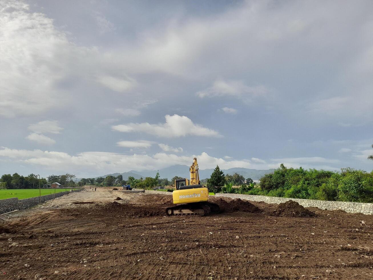 West Lombok Regency, Indonesia - February 4, 2024. Outdoors, a Backhoe is at work leveling the ground for a housing site, with a blue sky in the background. photo