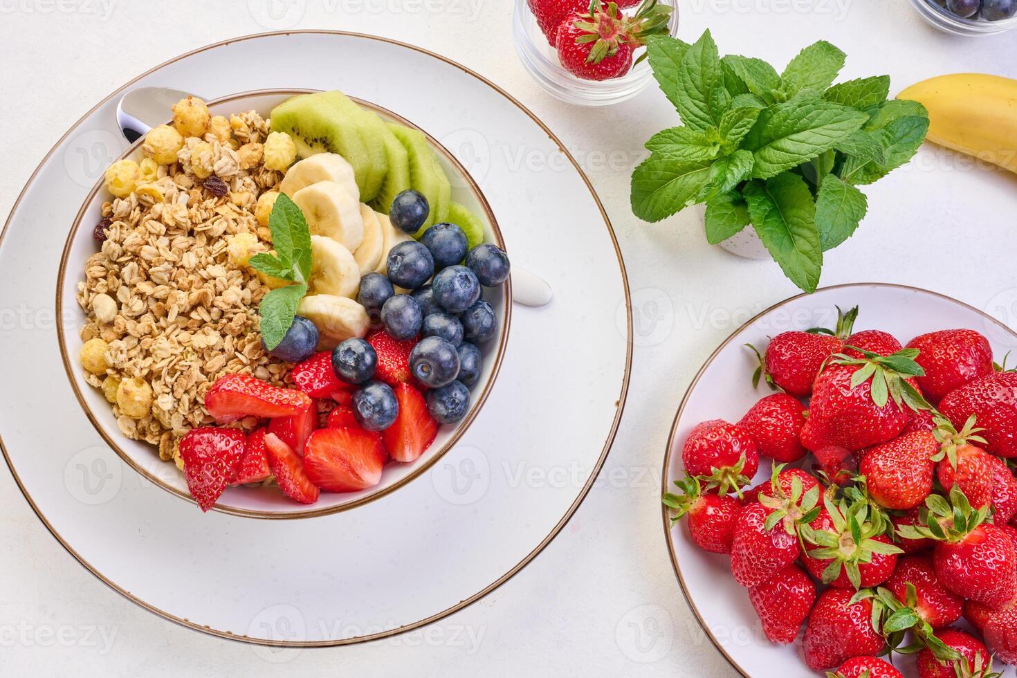 Granola with strawberries, kiwi, banana and blueberries in a round plate on a white table. Healthy and tasty food photo