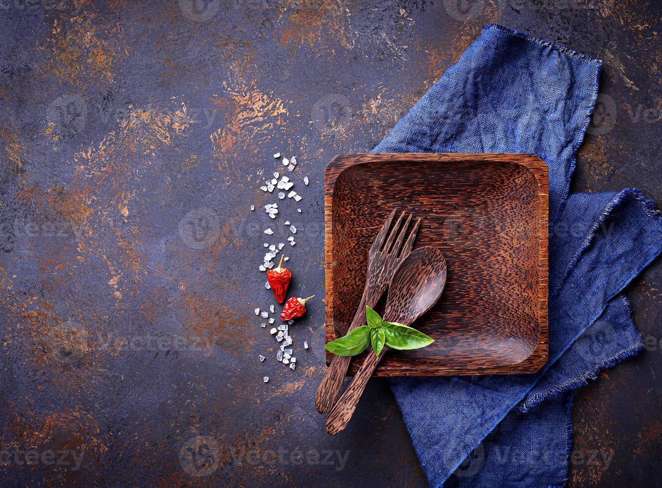 Empty wooden plate, cutlery, salt, pepper and basil photo
