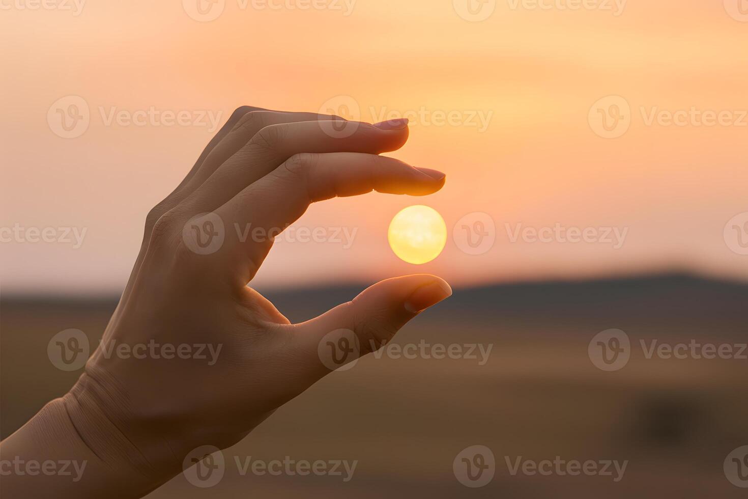 Hand delicately holds small, bright sun against warm, open landscape photo