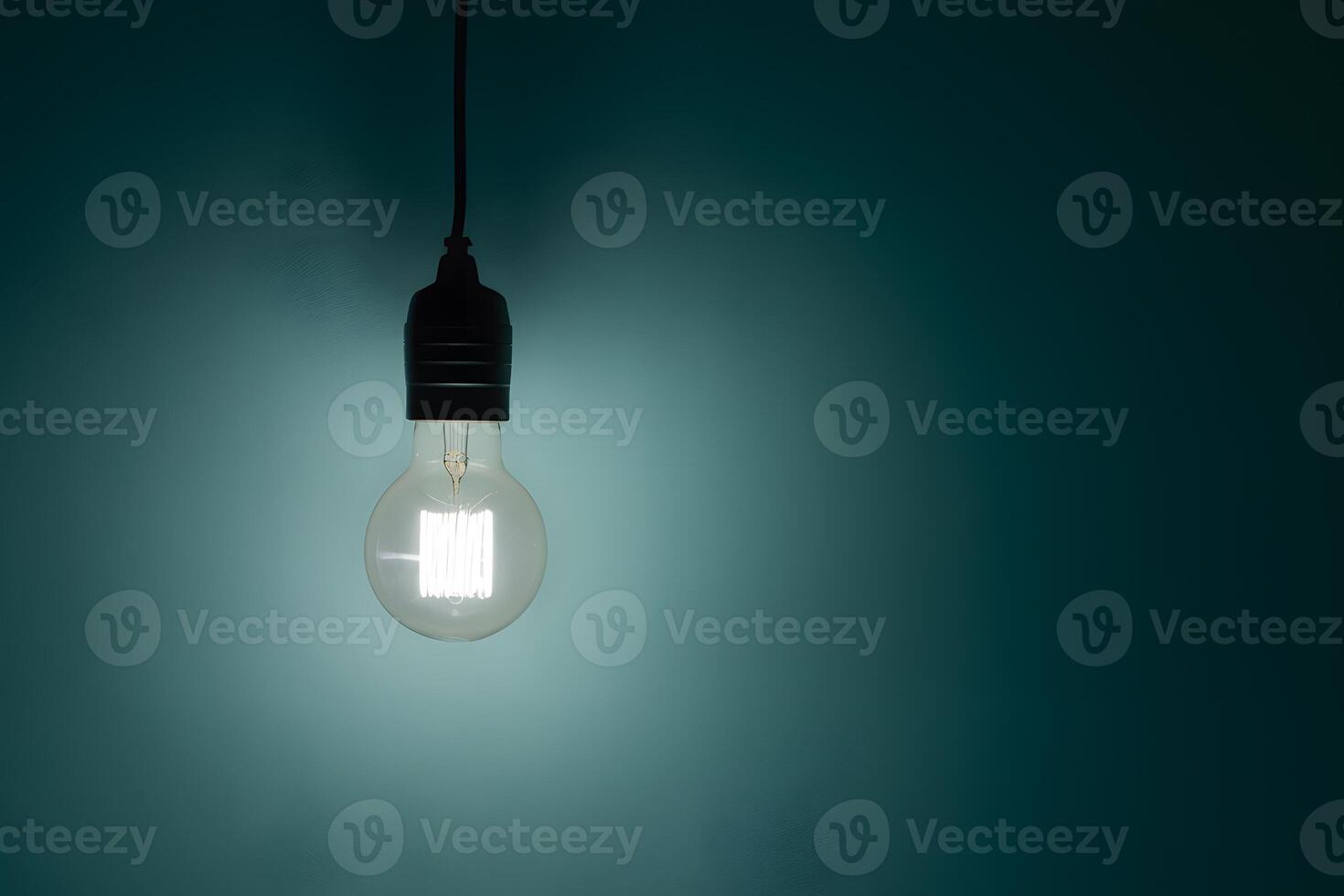 Illuminated light bulb hanging against a teal backdrop, casting a soft glow photo
