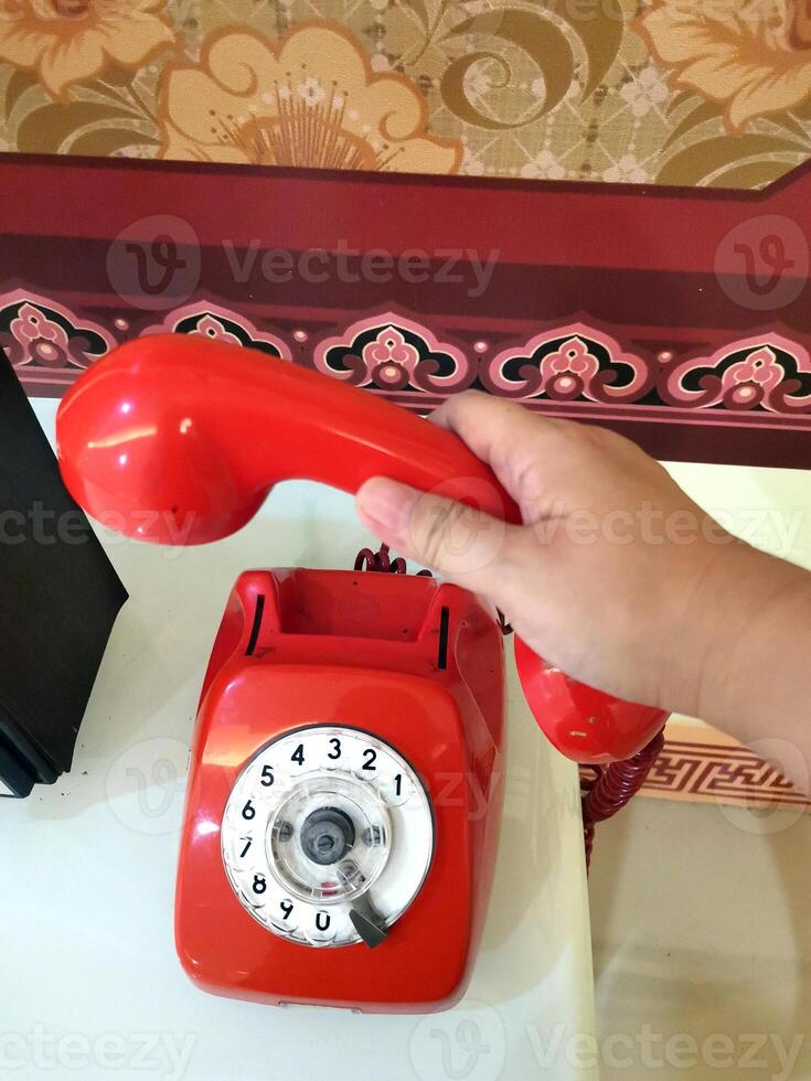 A person picks up a red telephone receiver to make or receive a telephone call with someone. Red rotary telephone with cable. photo