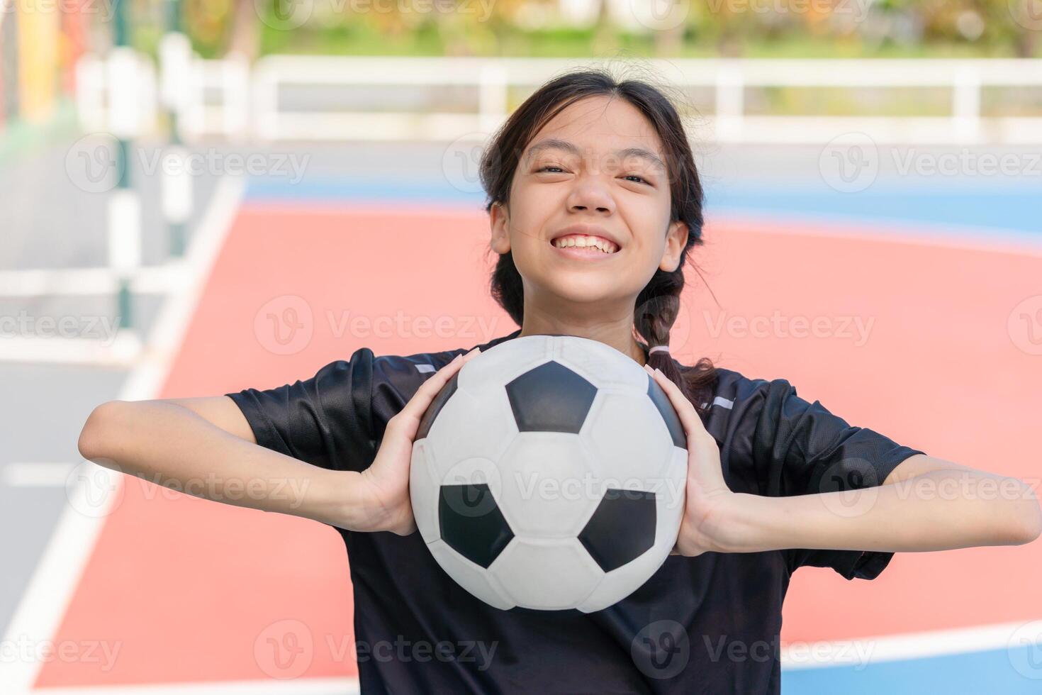 Cheerful kid girl with a soccer ball, Asian child girl playing football in the urban outdoor futsal court photo