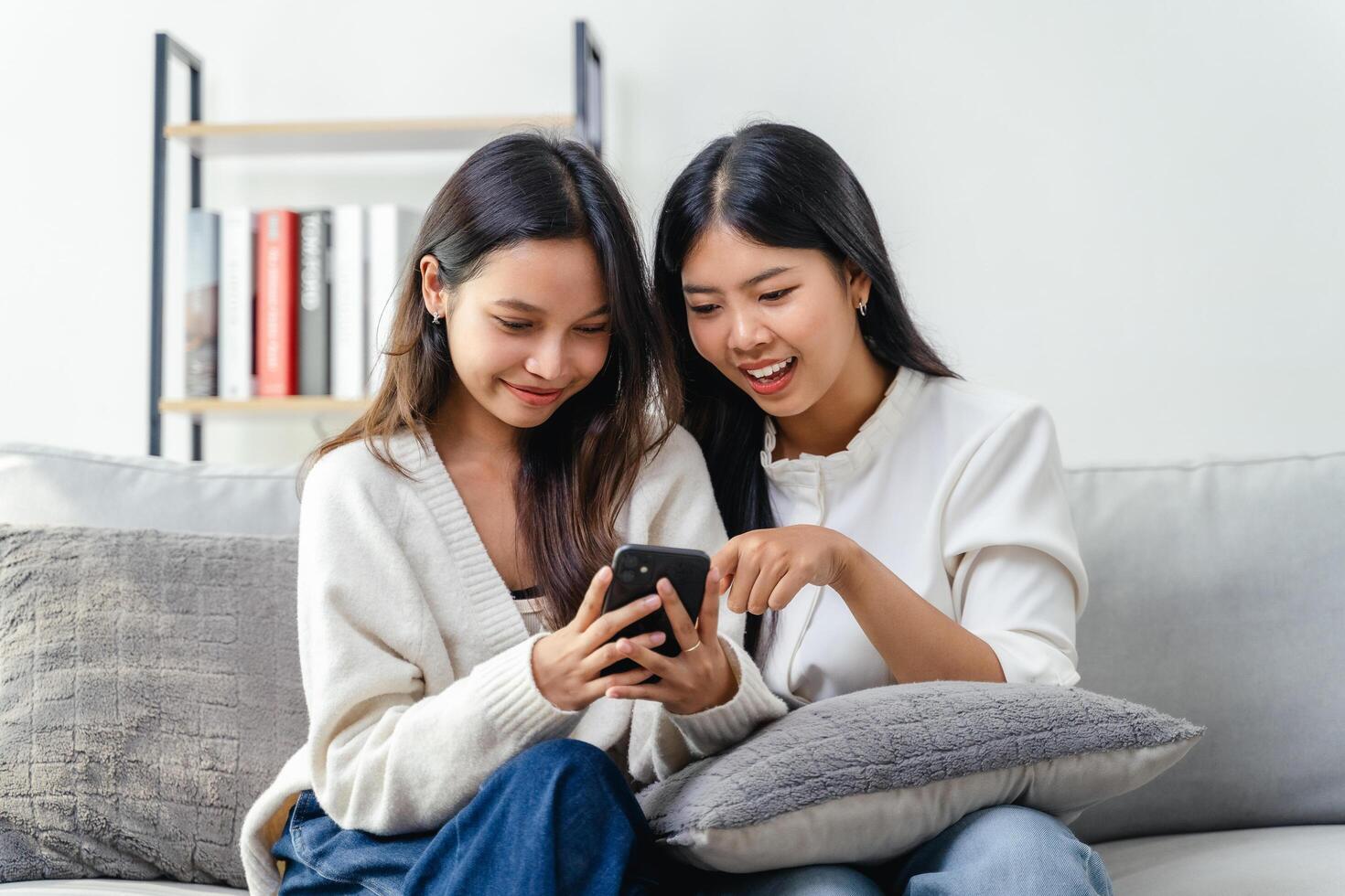 Two women sitting on a couch, using and looking at a cell phone photo